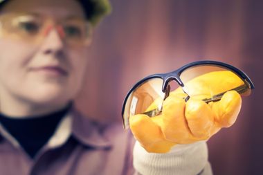 Person in safety glasses holds yellow citrus slices in gloved hand for inspection