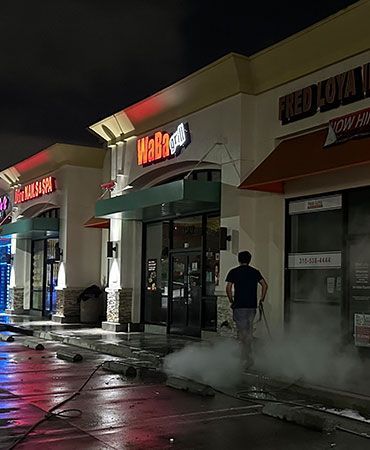 A man is cleaning the sidewalk outside of a mall at night.