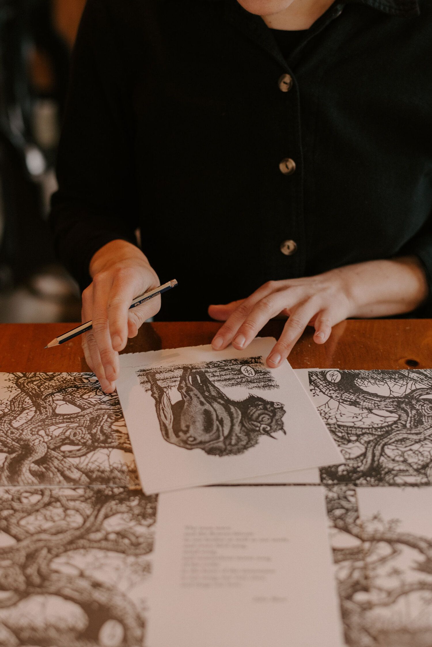 Hands arranging printed artwork on a patterned table, with a pen in hand.