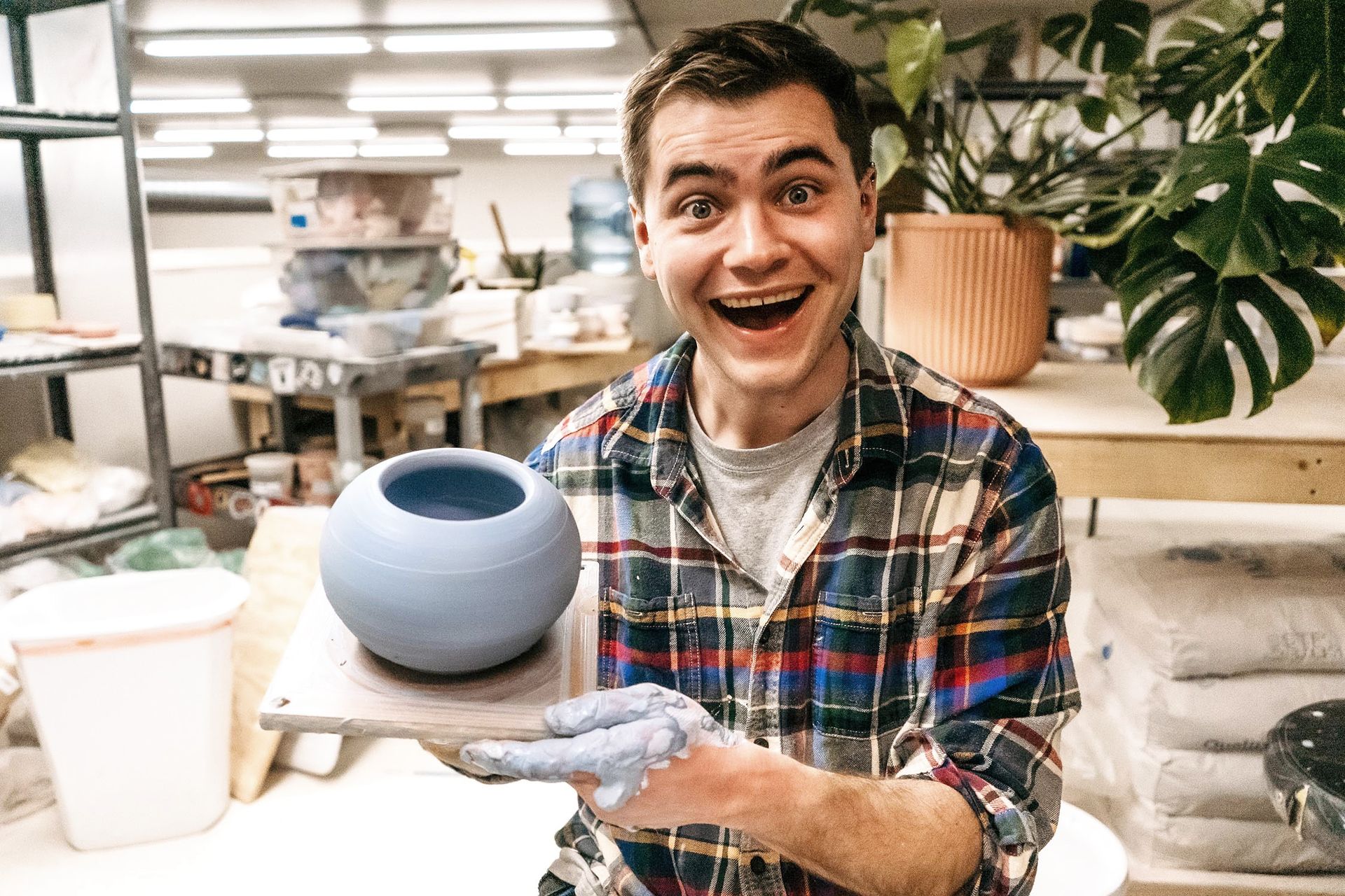 Smiling potter holding a blue ceramic vase in a pottery studio