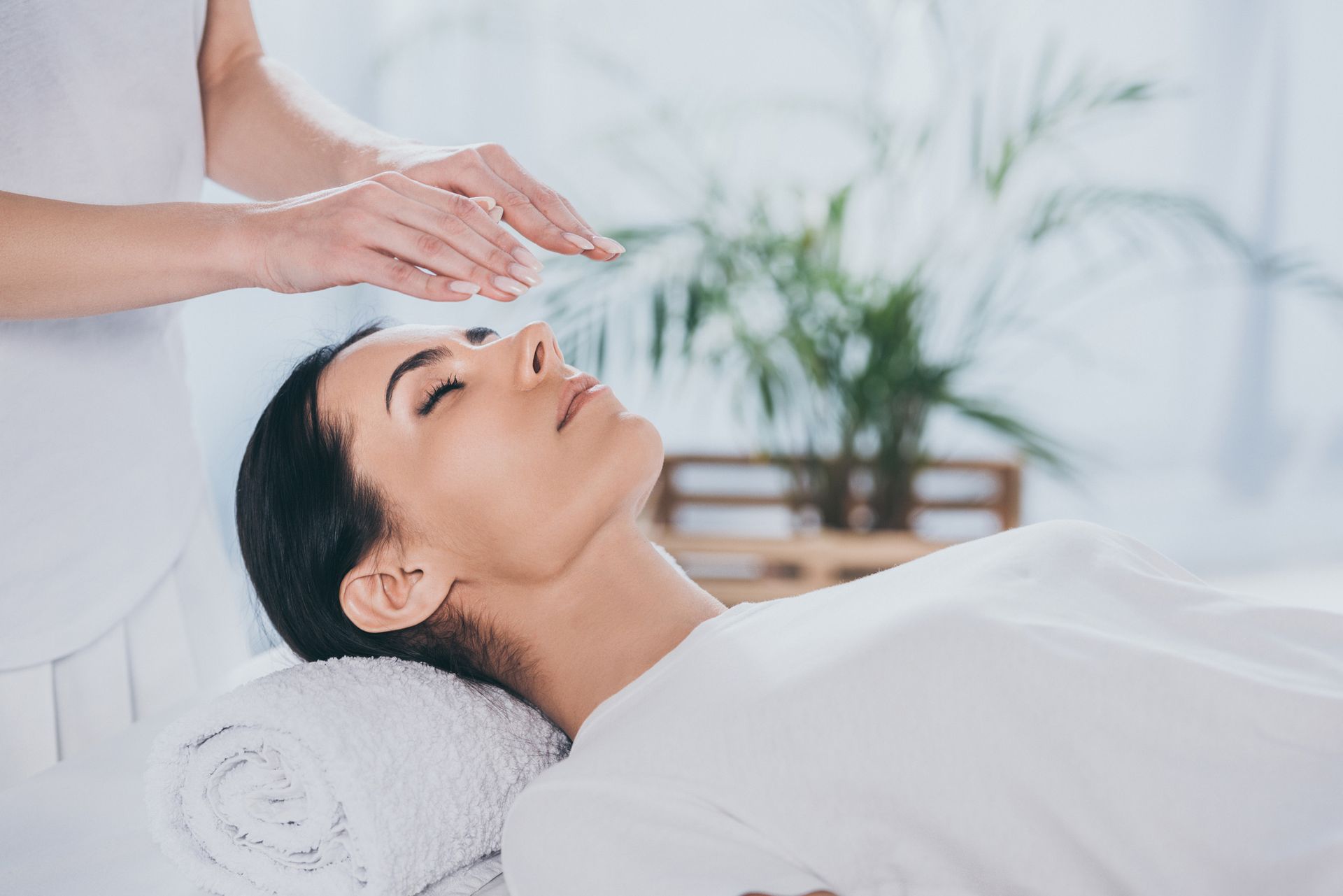 Woman receiving reiki treatment, hands above head, eyes closed, peaceful expression.