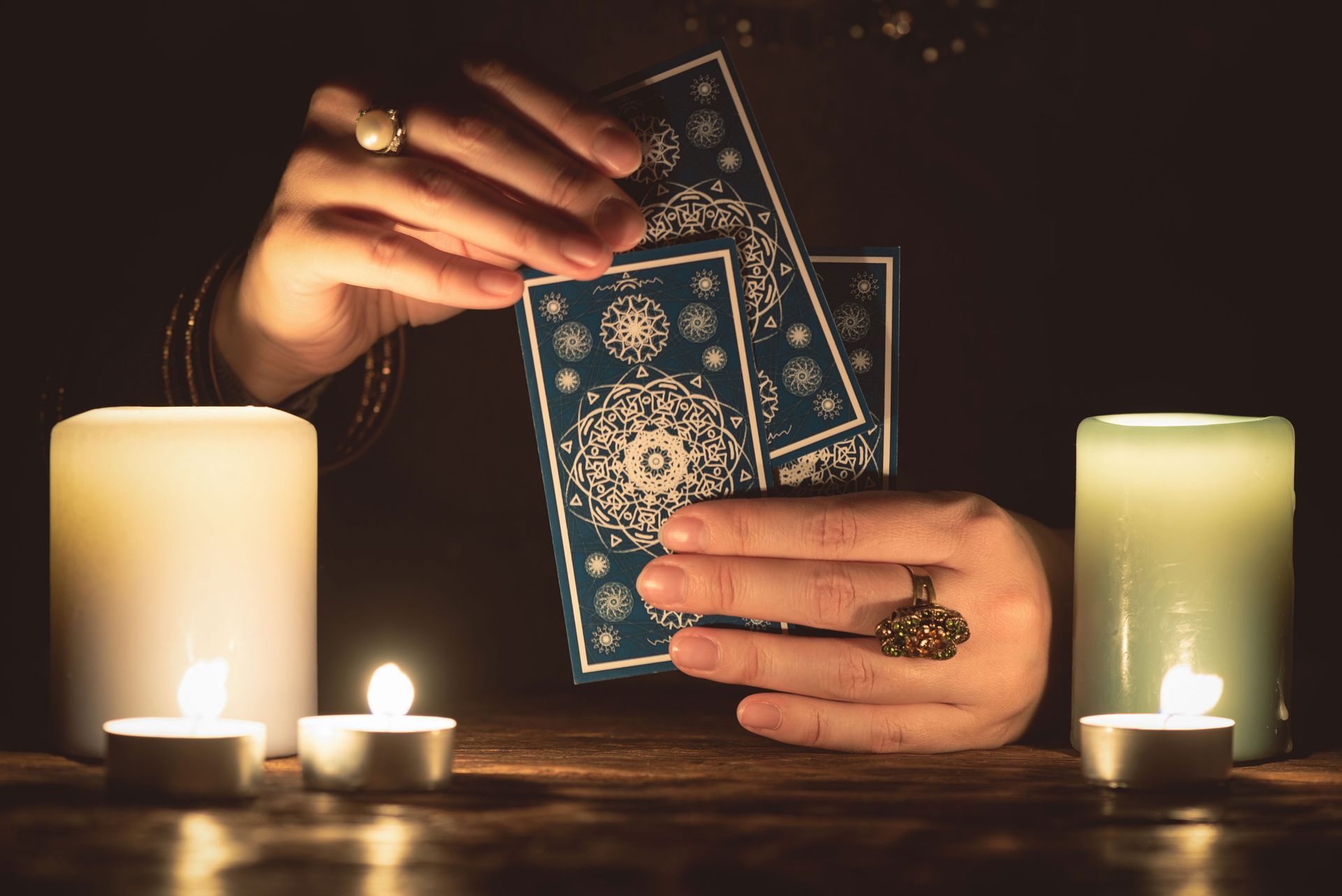 Hands holding tarot cards near lit candles. Dark setting.