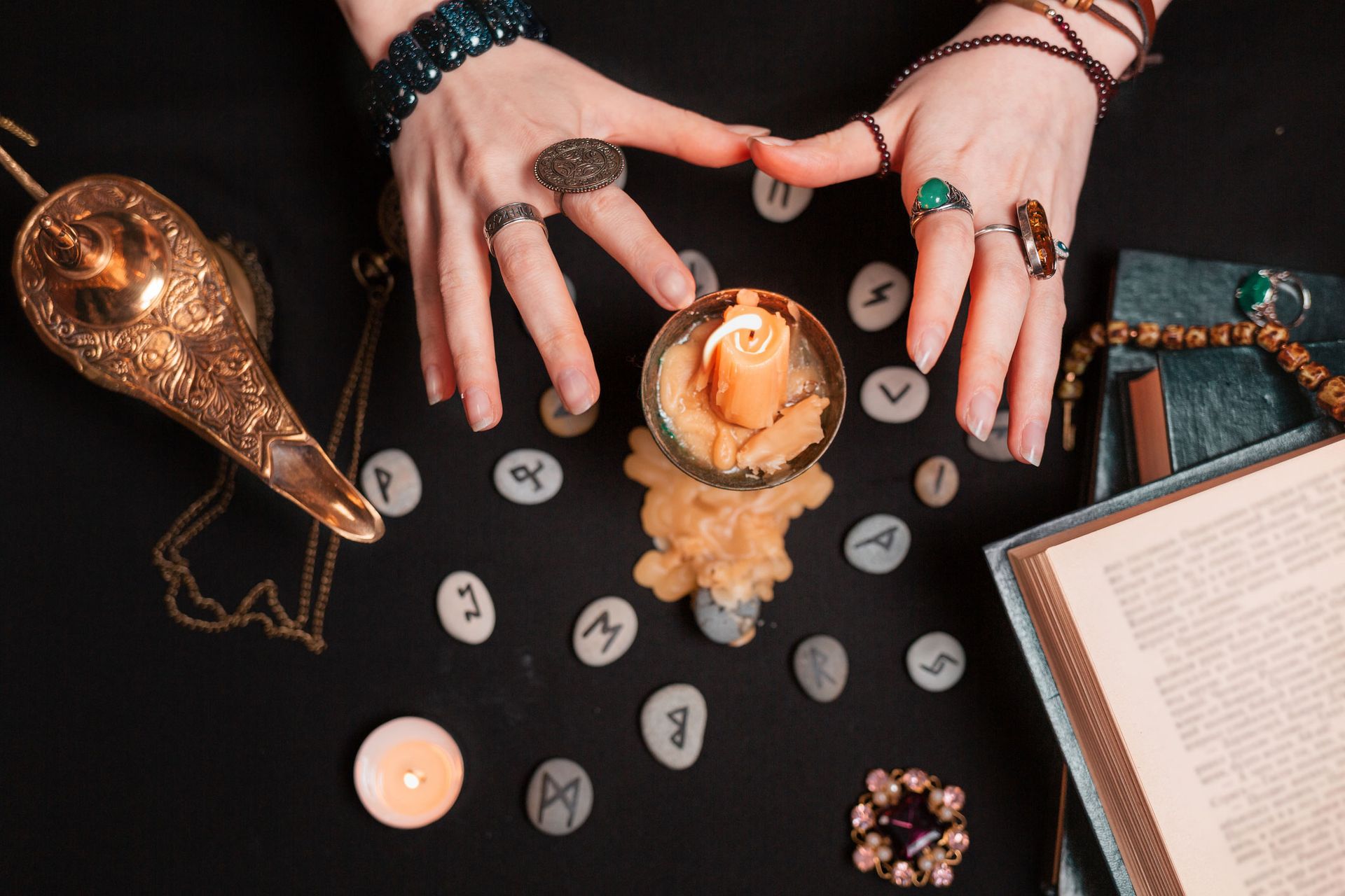 Hands with rings over candle and runes on black surface.