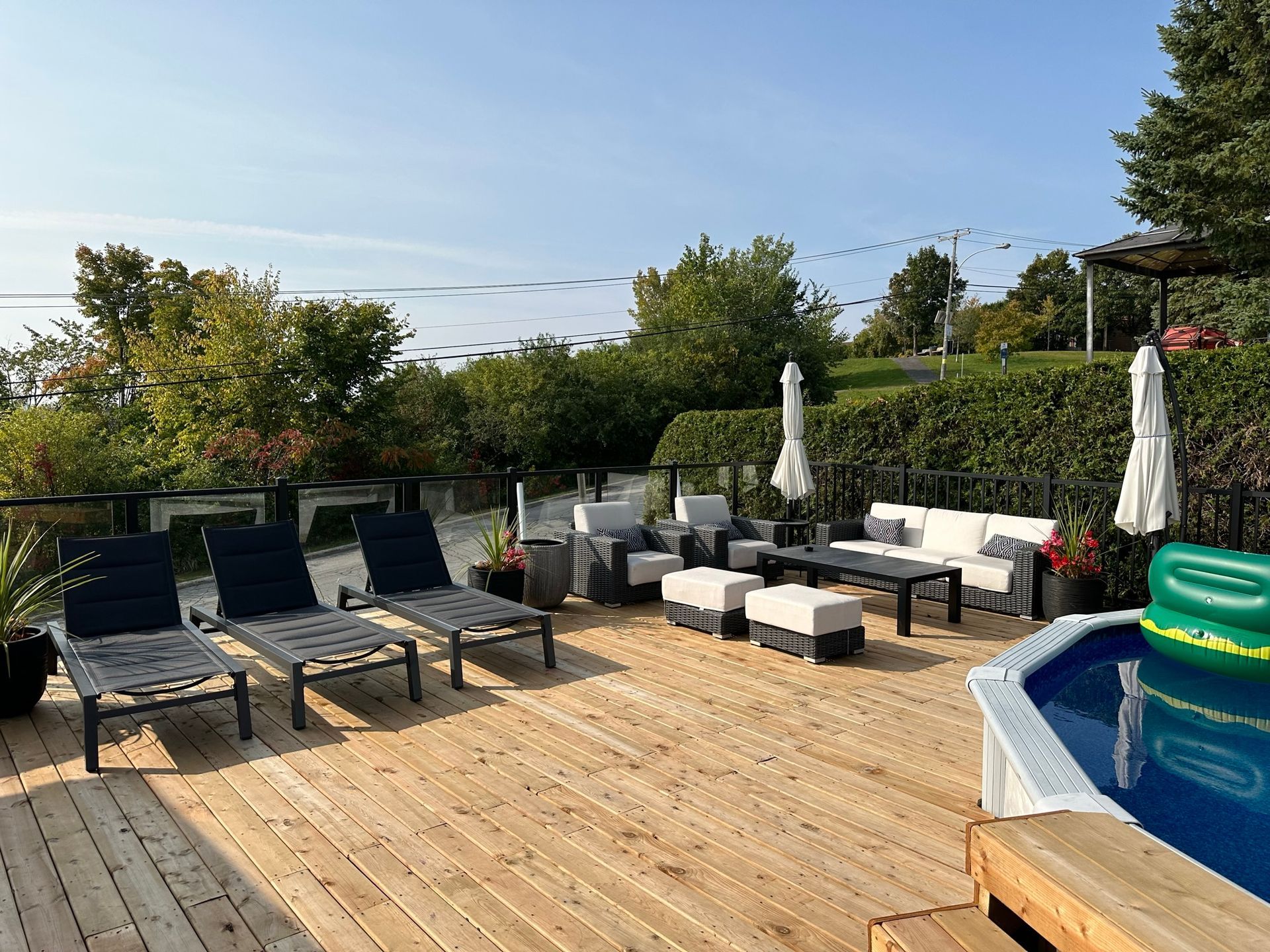 Une terrasse en bois avec des chaises, un canapé, des parasols et une piscine.