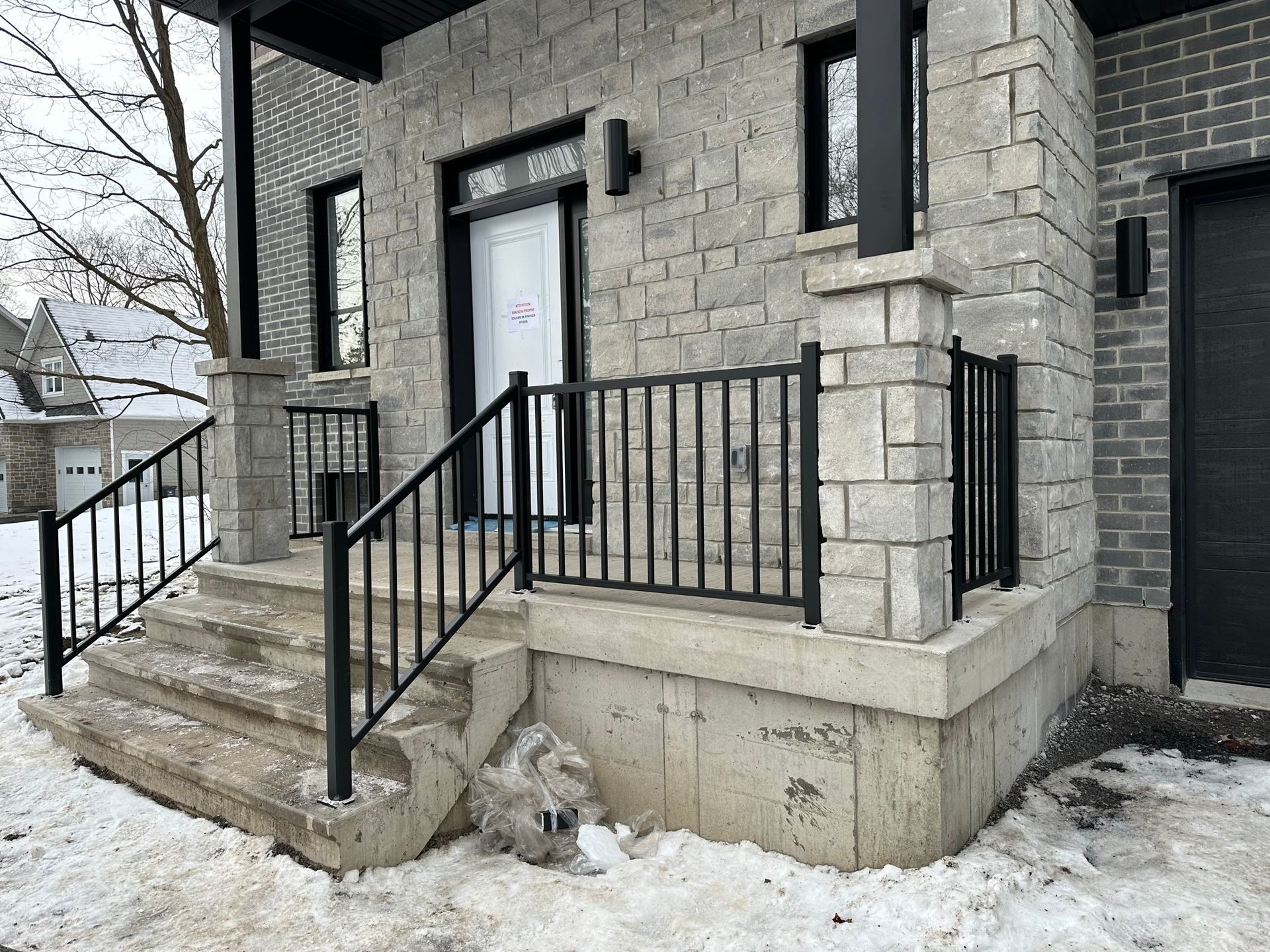 Une maison en briques avec une balustrade noire et des escaliers dans la neige.