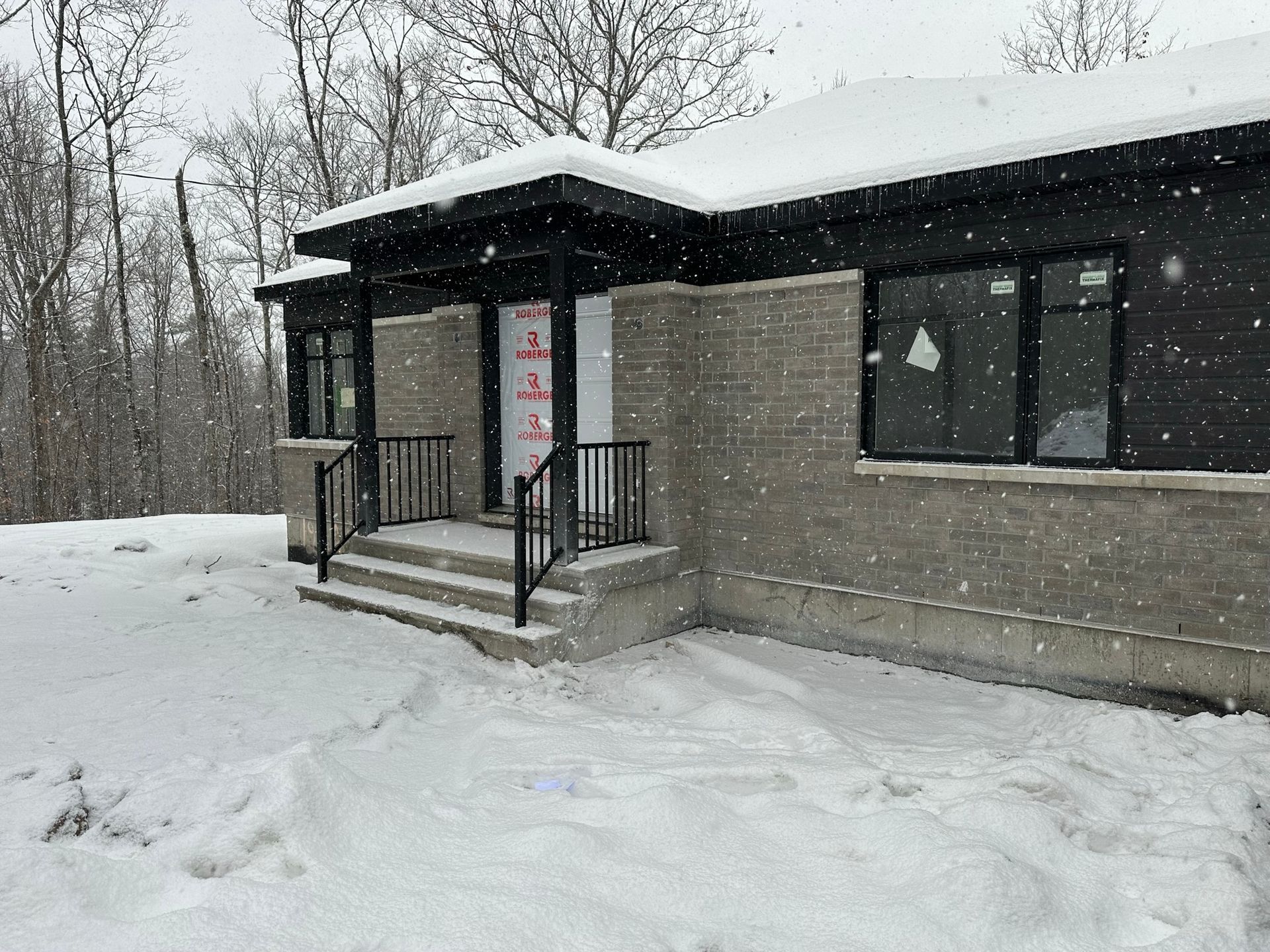 Une maison est couverte de neige et des arbres sont en arrière-plan.