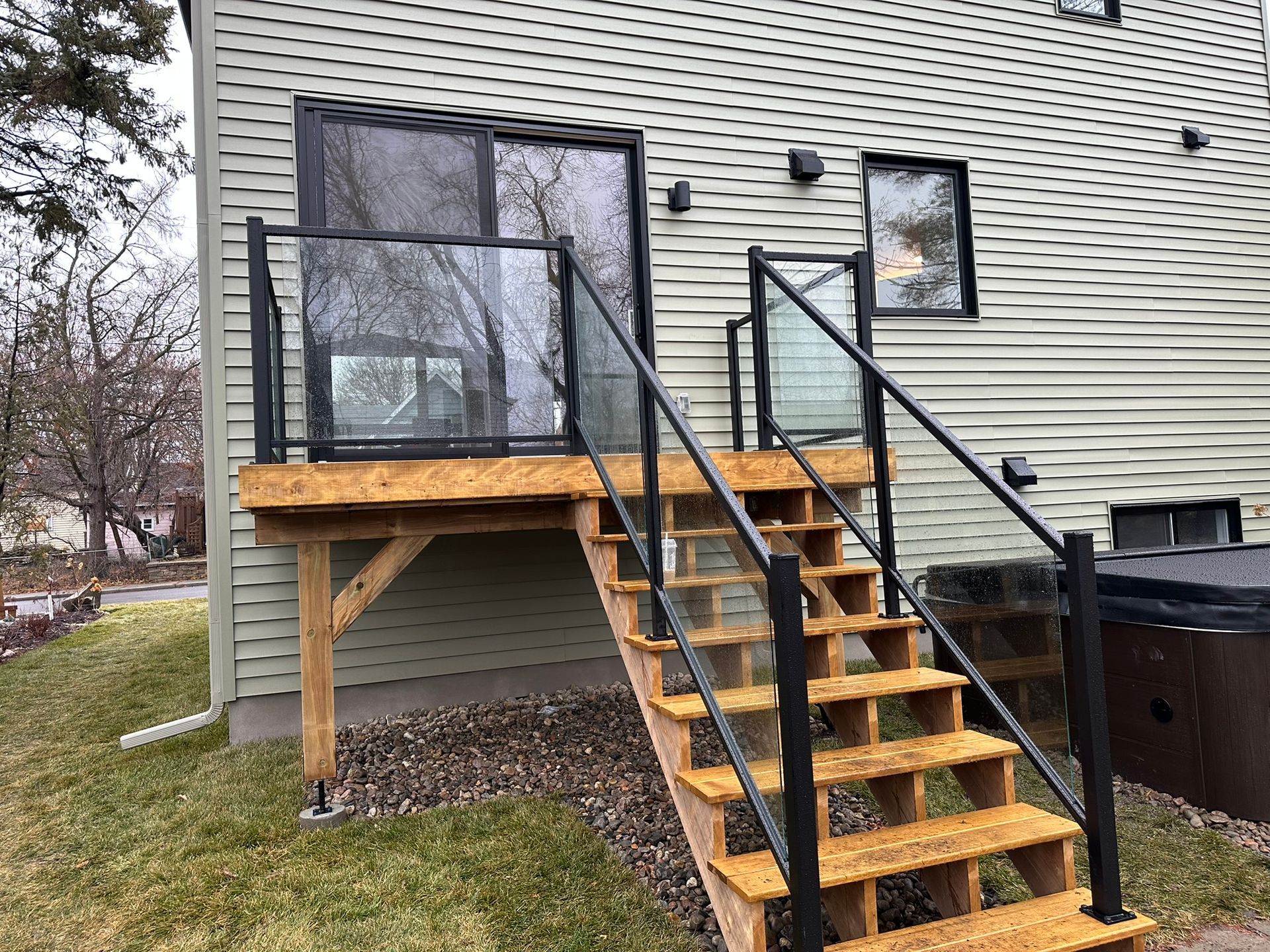 Une terrasse en bois avec des escaliers qui y mènent et une balustrade en verre.