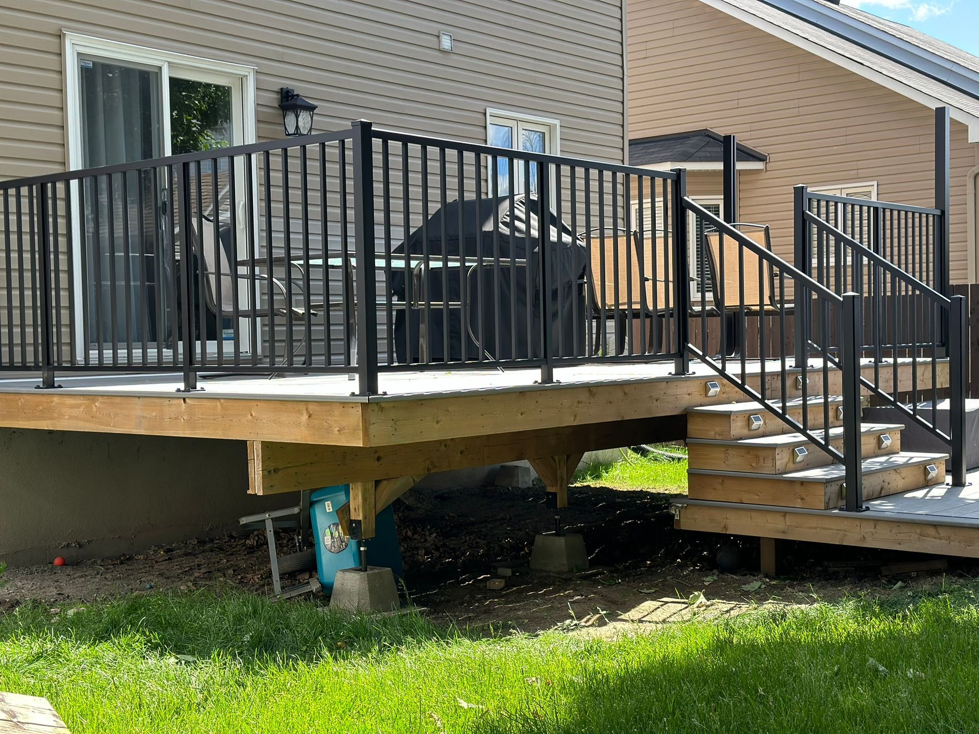 Une terrasse en bois avec des escaliers et une rampe en métal devant une maison.
