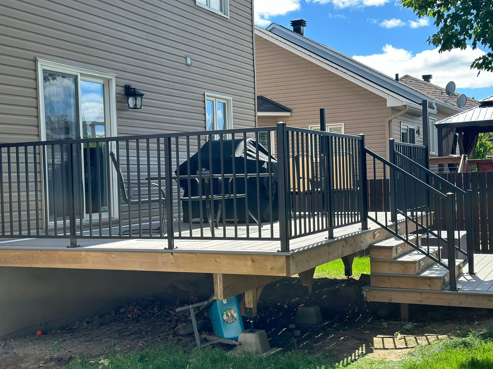 Une terrasse en bois avec des escaliers et une rampe en métal devant une maison.