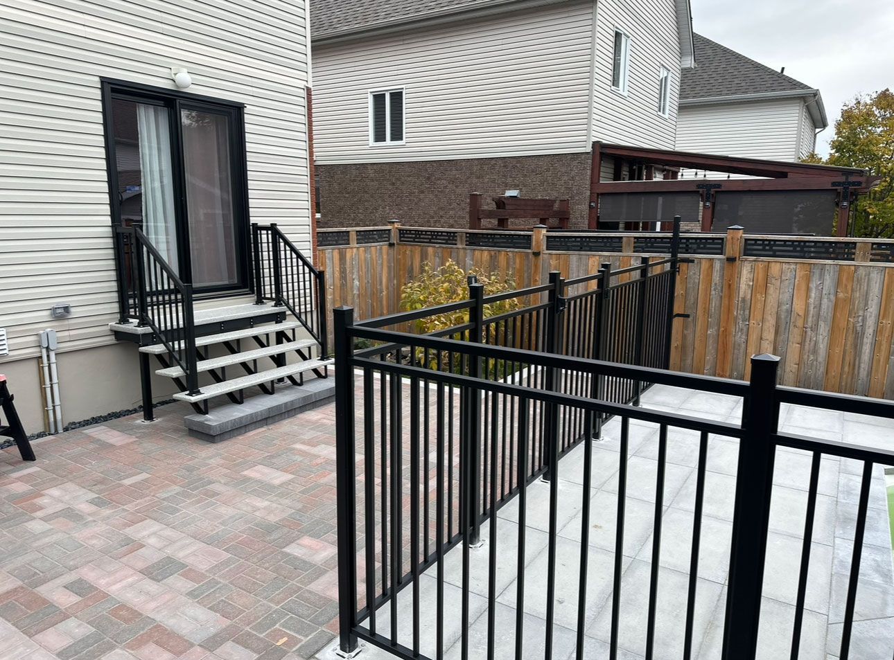 Un patio avec des escaliers et une clôture noire devant une maison.