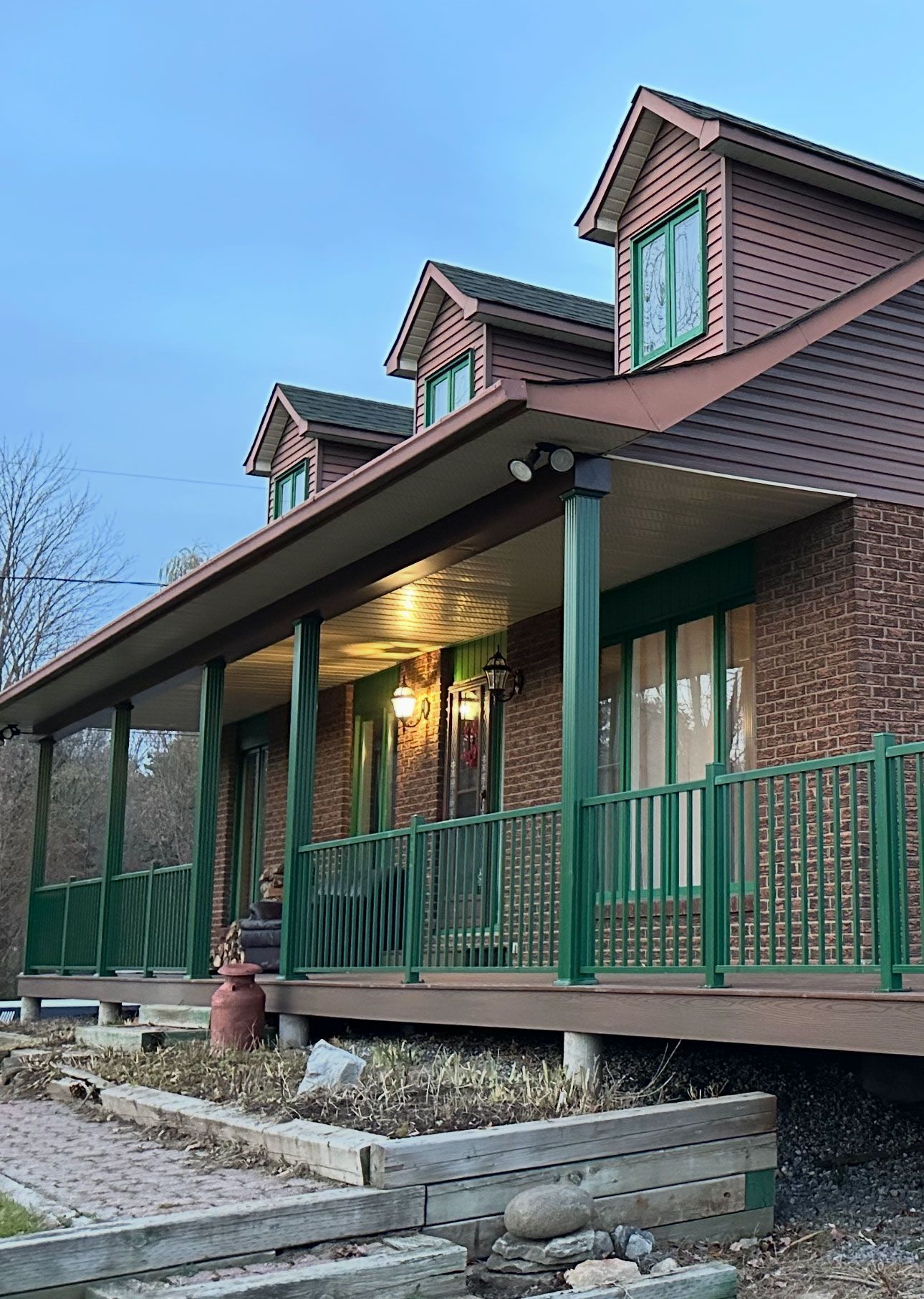 Une maison en briques avec un grand porche et une balustrade verte.