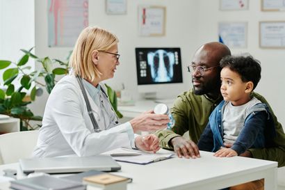 A doctor is talking to a man and a child at a table.