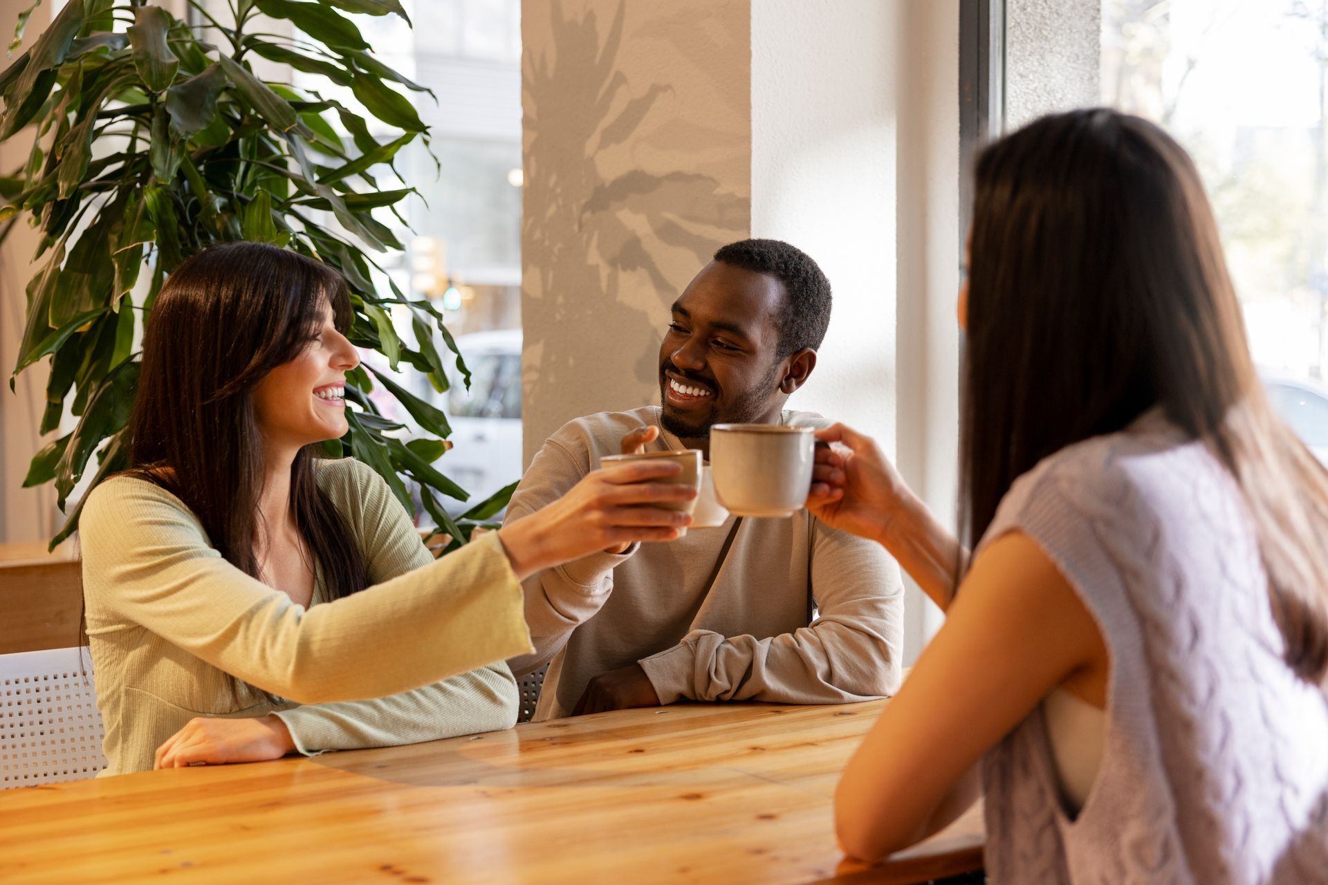 A group of people are sitting at a table toasting with cups of coffee.