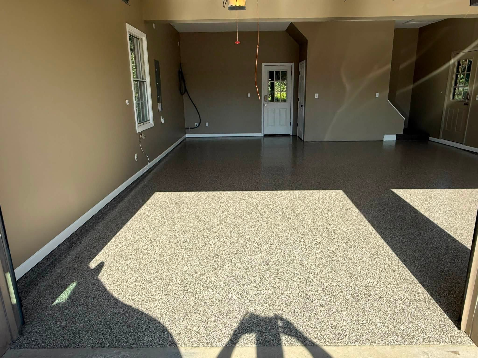 Empty garage interior with speckled floor, open door, and sunlight streaming in through the front opening.