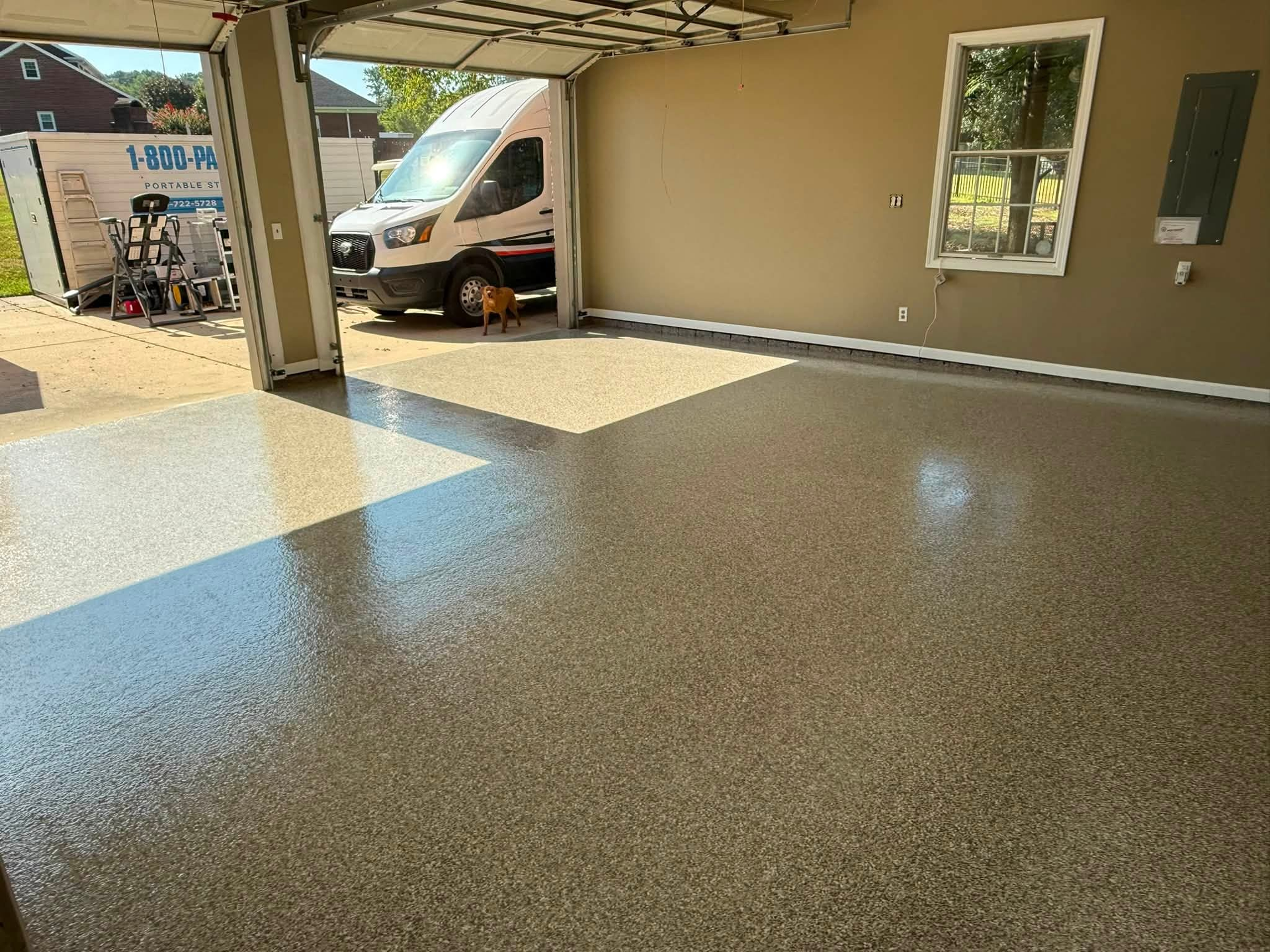 Covered driveway with glossy speckled floor and a van parked beside a beige house.