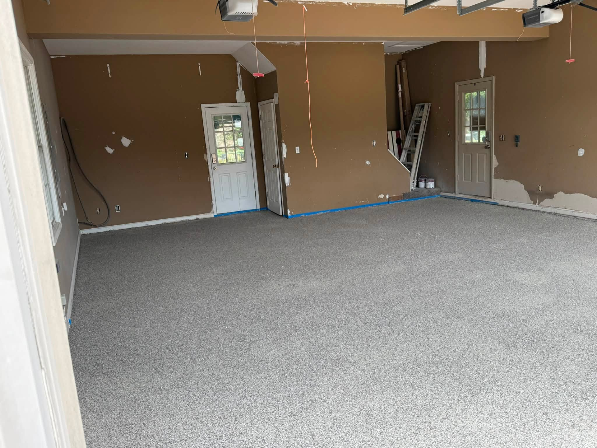 Empty unfinished garage with tan walls, white doors, and gray carpet flooring
