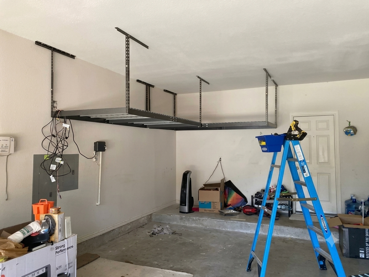 Garage under construction with a suspended black metal frame, blue ladder, and tools scattered on the floor.