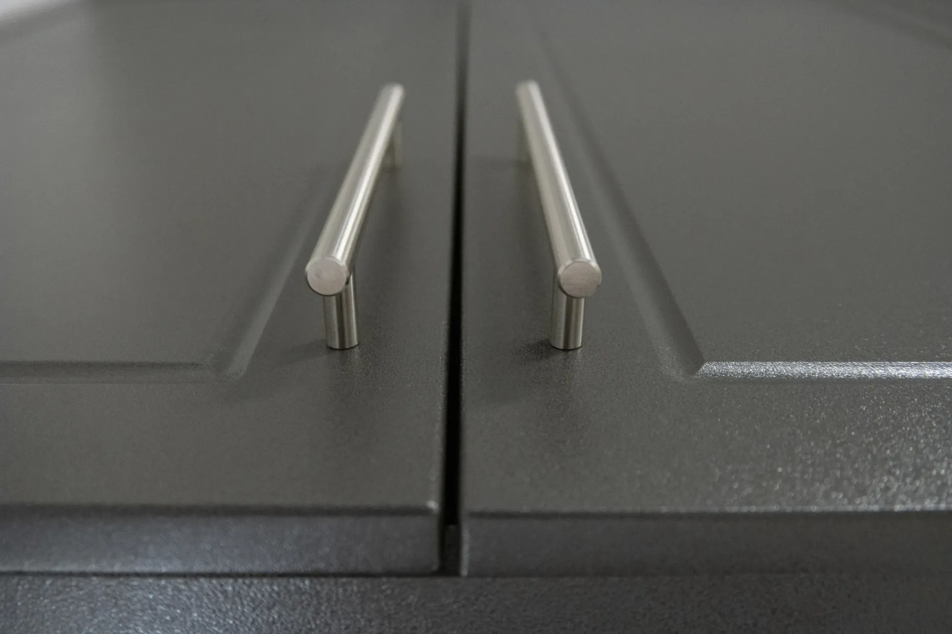 Close-up of two gray cabinet doors with silver bar handles.