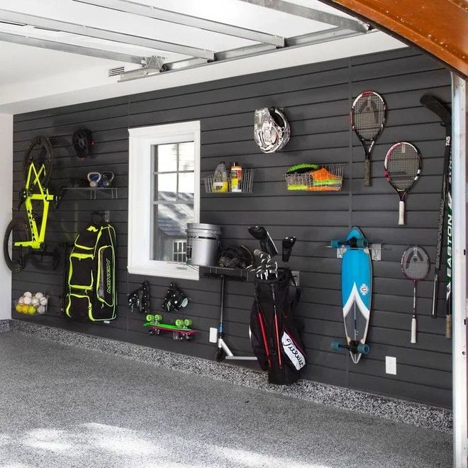 Garage wall with hanging sports gear, backpacks, golf clubs, and tennis rackets on dark slatwall.