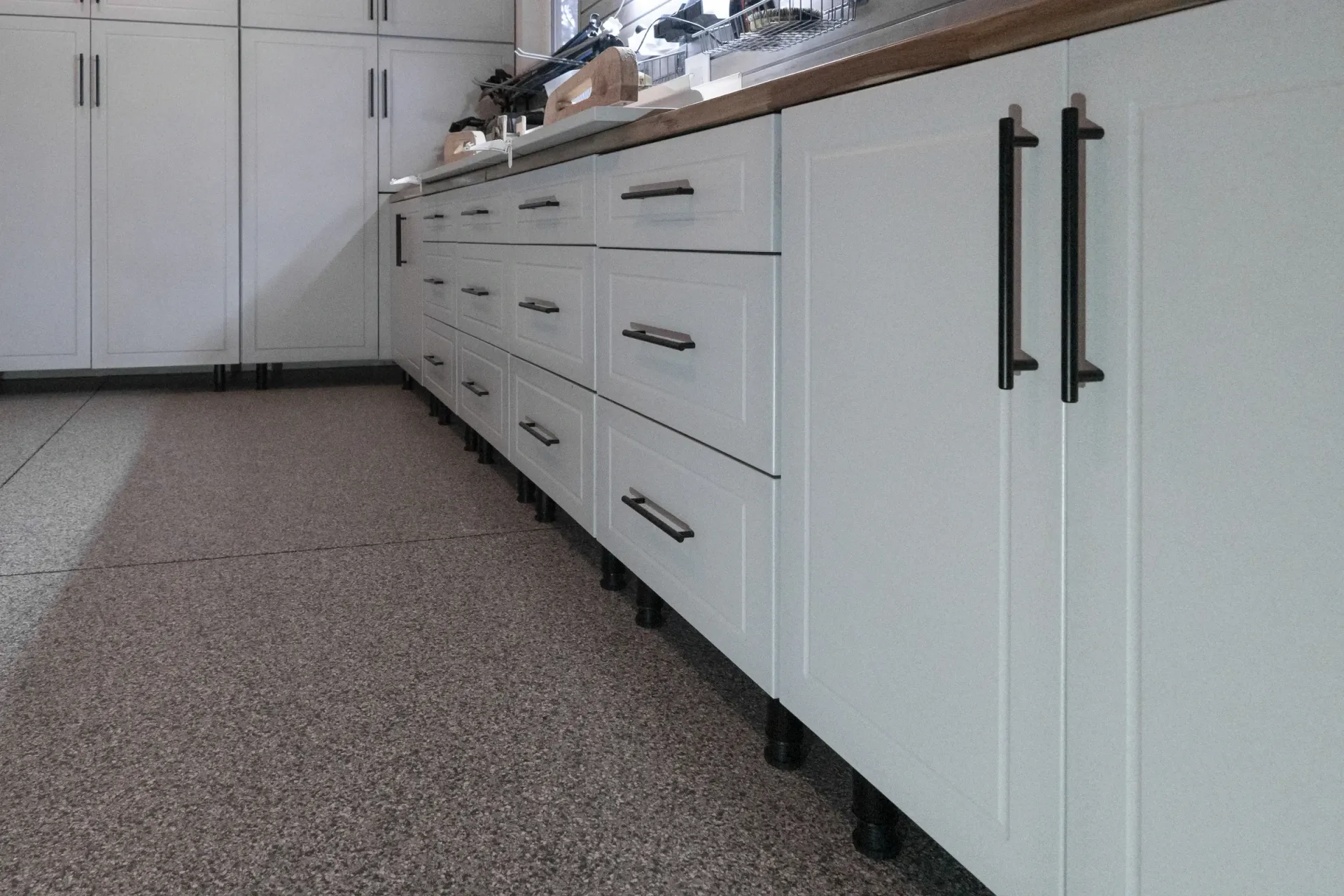 White kitchen cabinets with black handles along a speckled floor, low-angle view