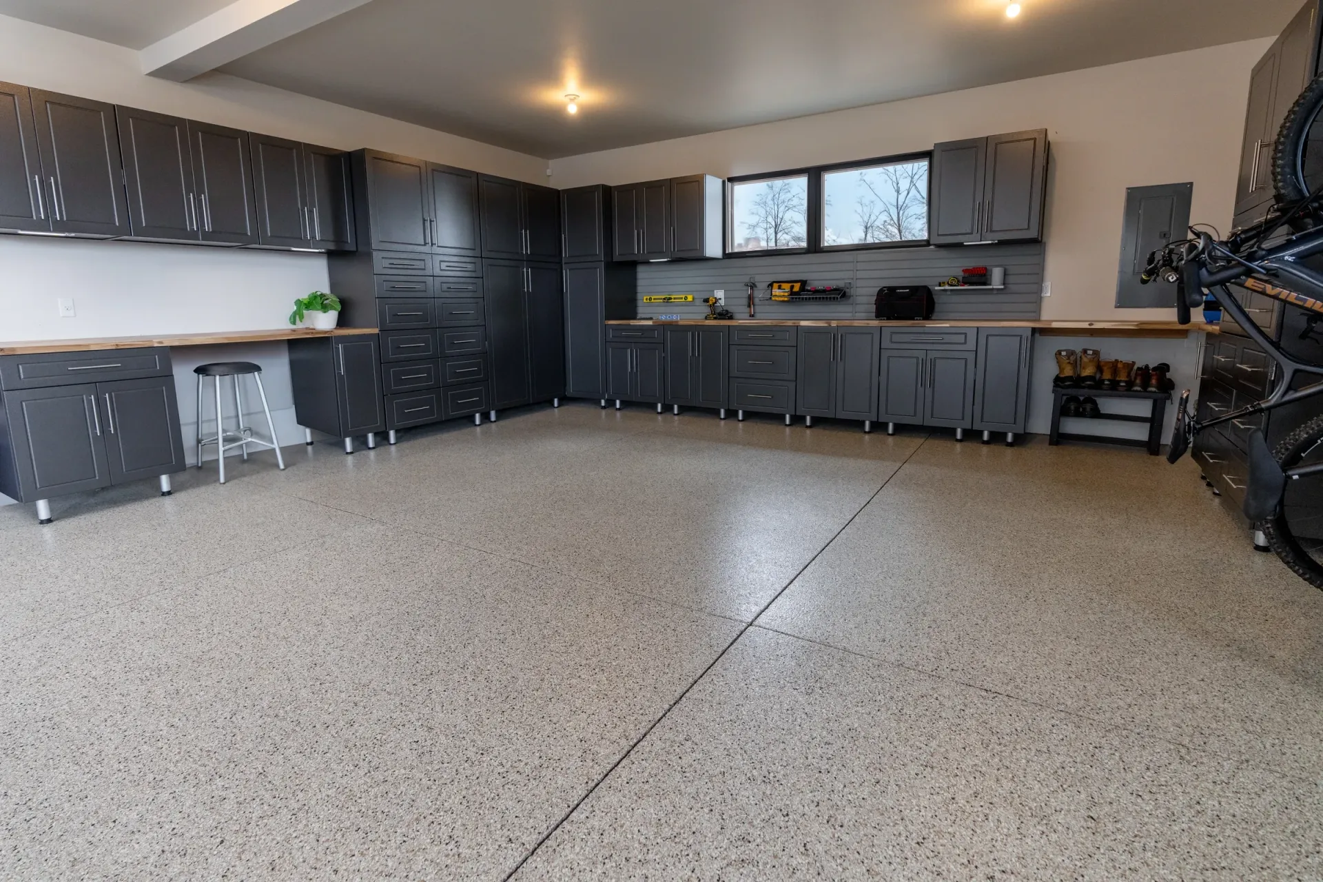 Spacious garage with gray cabinets, workbench, and speckled concrete floor under ceiling lights