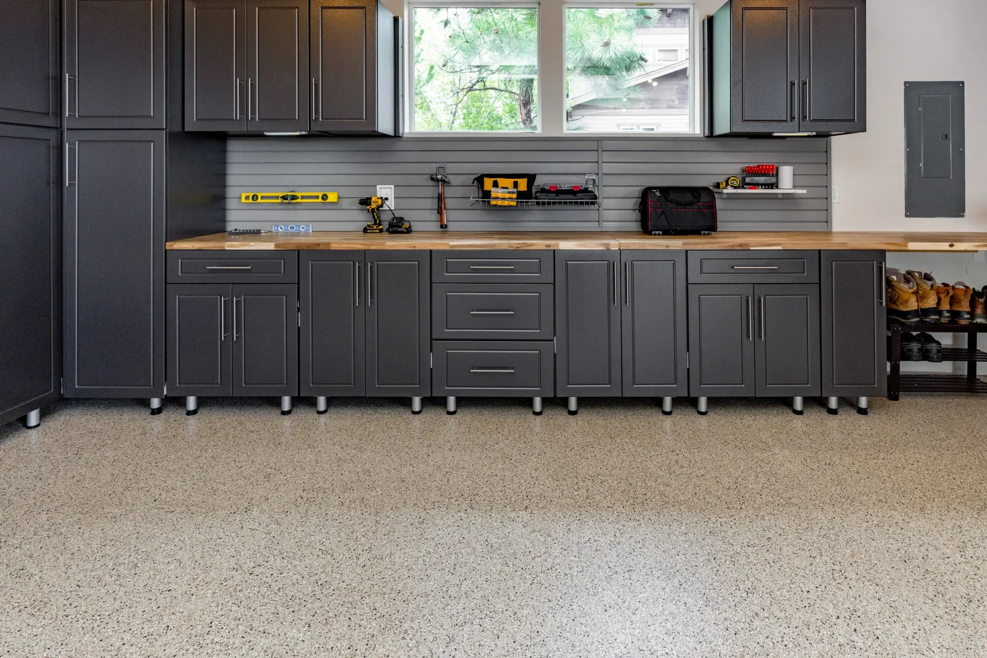 Gray garage with long workbench, cabinets, tools, and a speckled epoxy floor under a window.