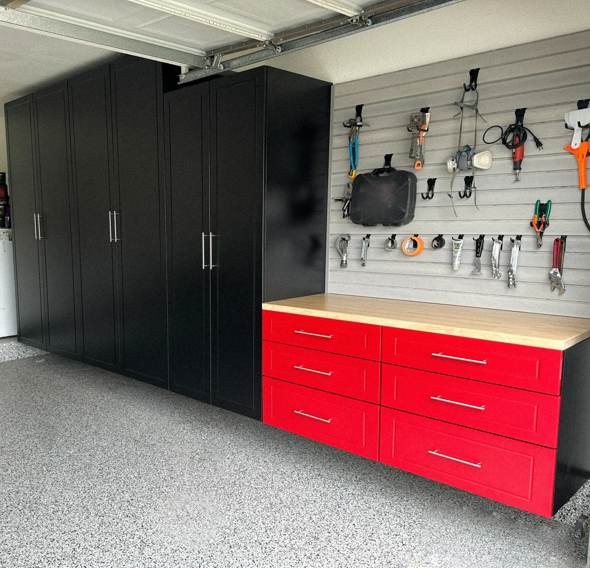Garage wall with black cabinets and red drawers beneath a pegboard of tools and supplies.