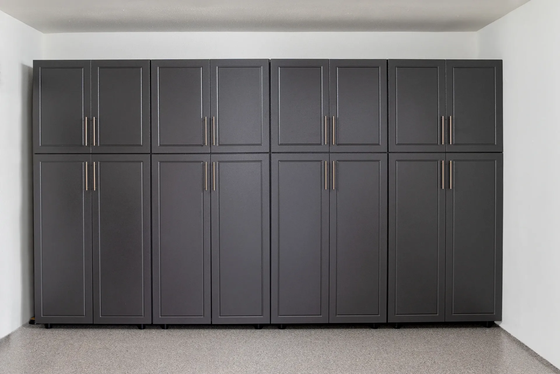 Dark gray built-in cabinets line a white garage wall above a speckled floor.