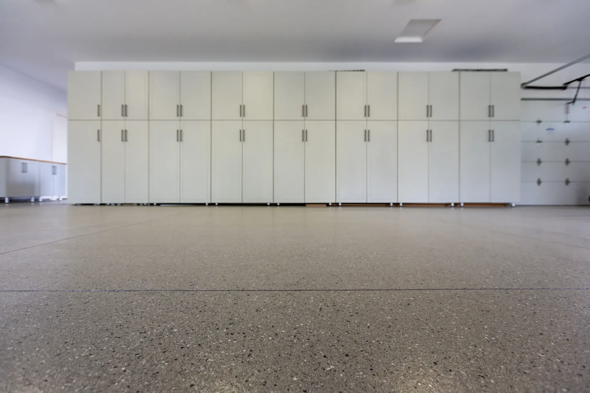 Empty garage with white storage cabinets along the wall and speckled concrete floor