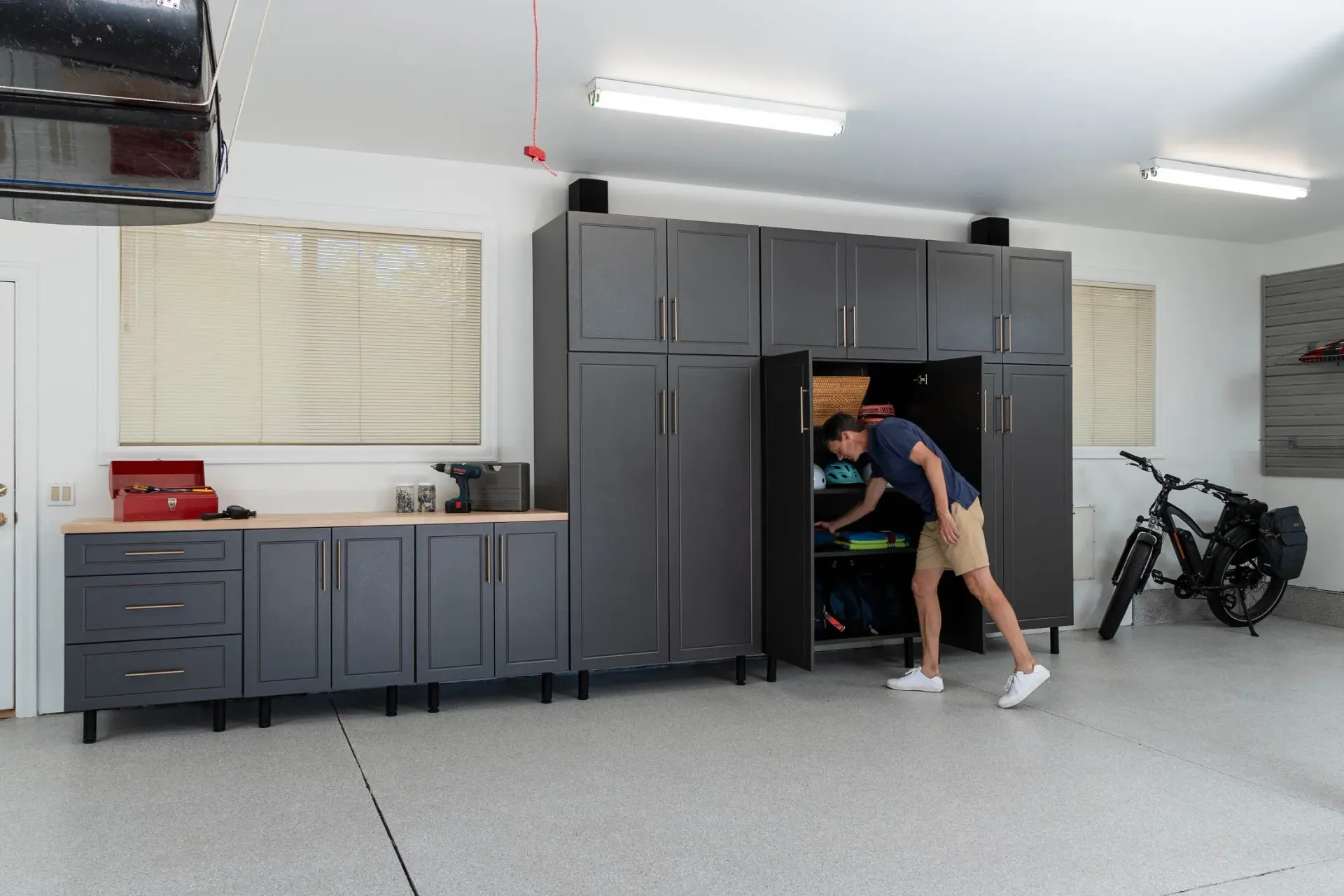 Person reaching into a dark gray garage storage cabinet beside a motorcycle in a tidy workshop