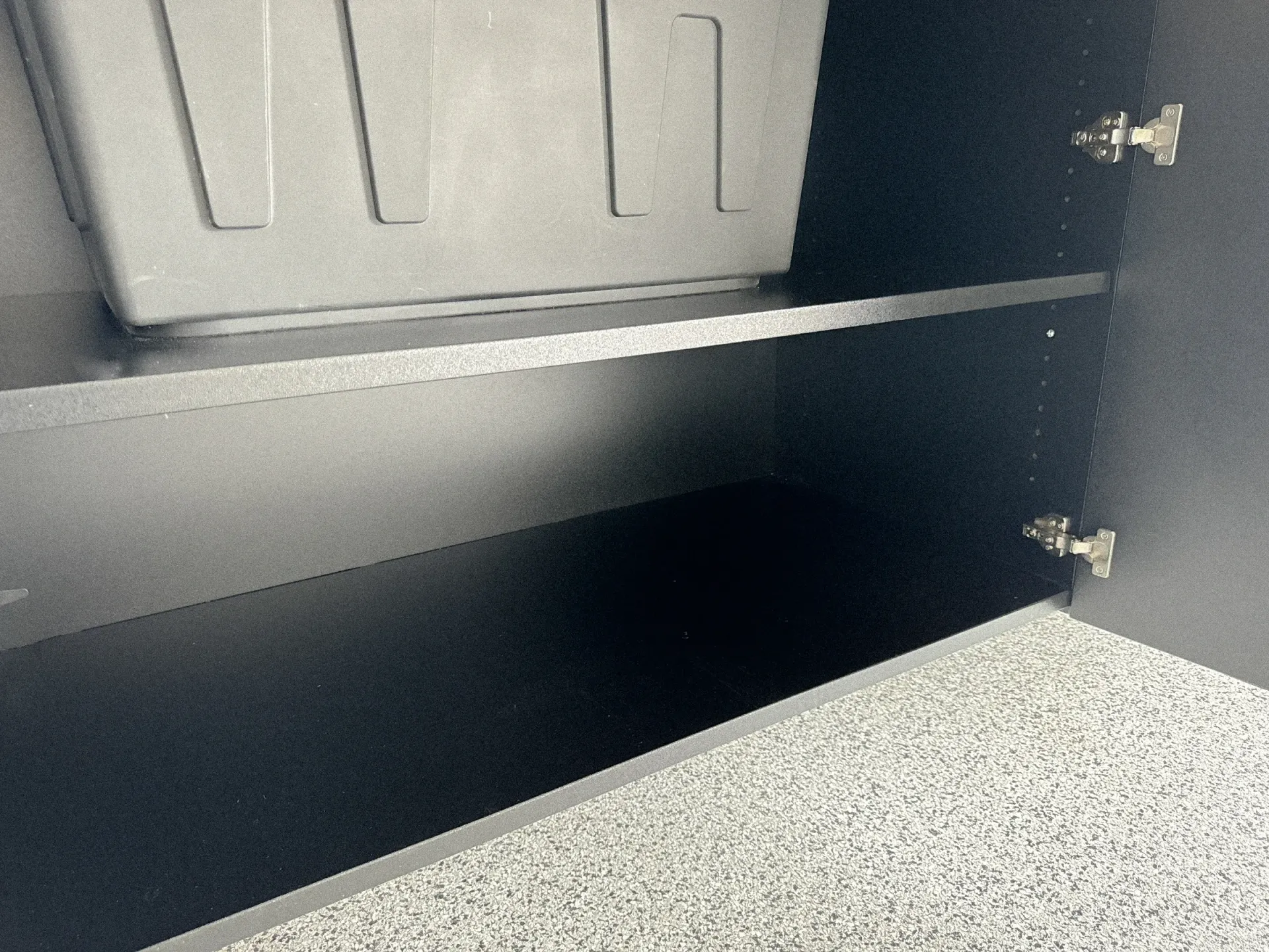 Open cabinet with a black shelf and gray speckled countertop inside.