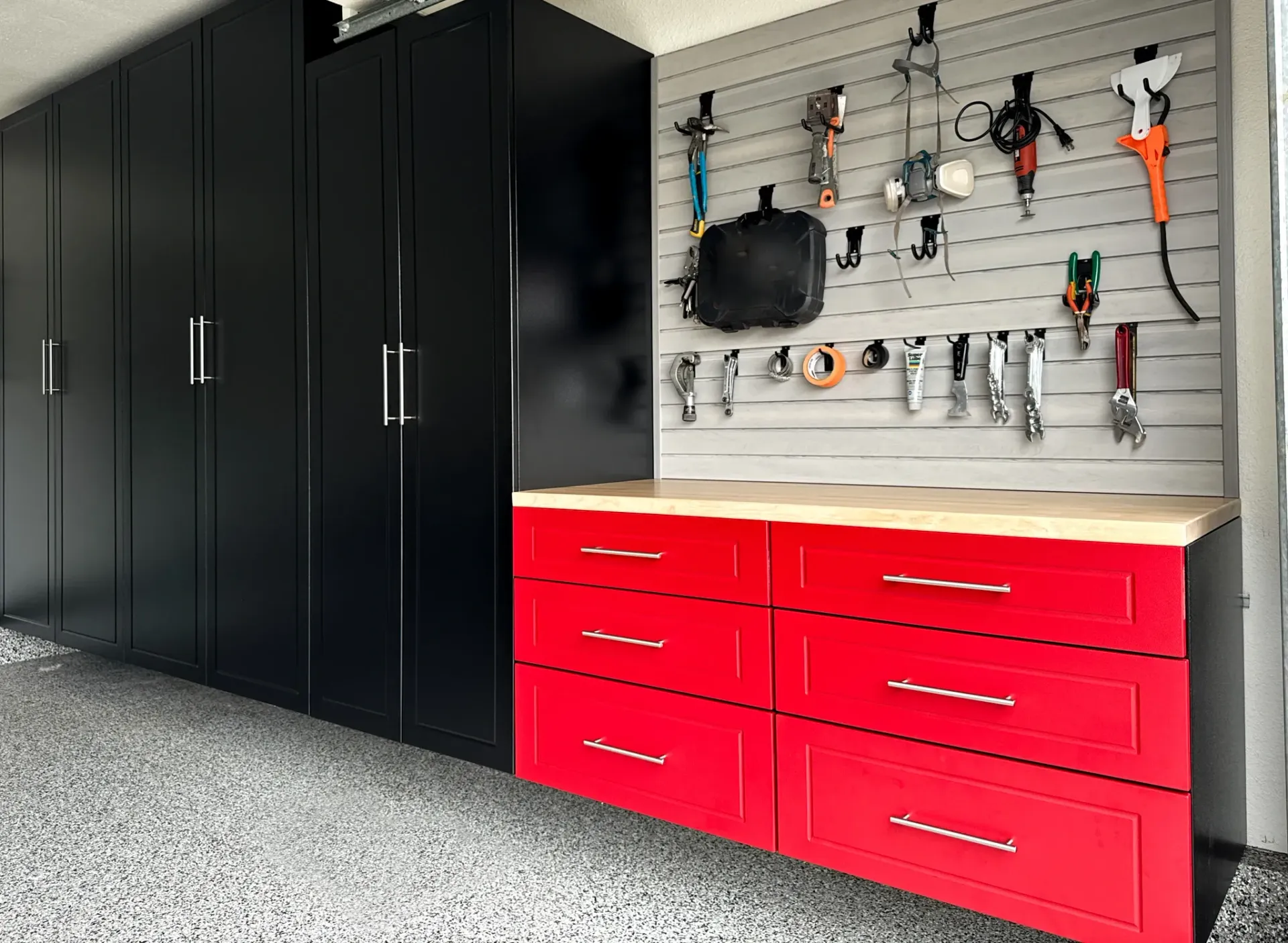 Garage storage cabinets with black upper cabinets and red lower drawers beside a wall tool rack.