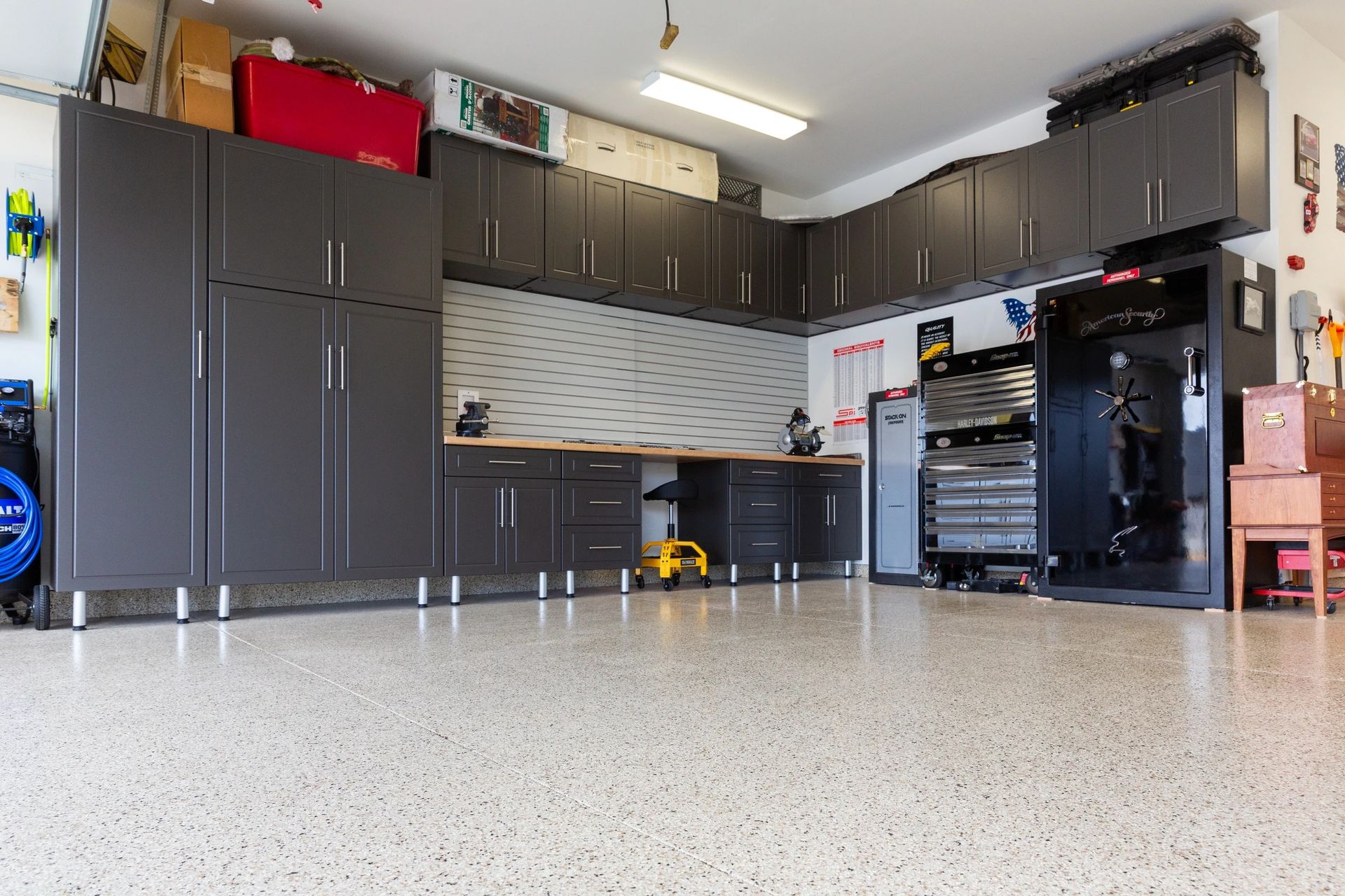 Spacious garage with dark cabinets, speckled floor, workbench, and open storage shelves
