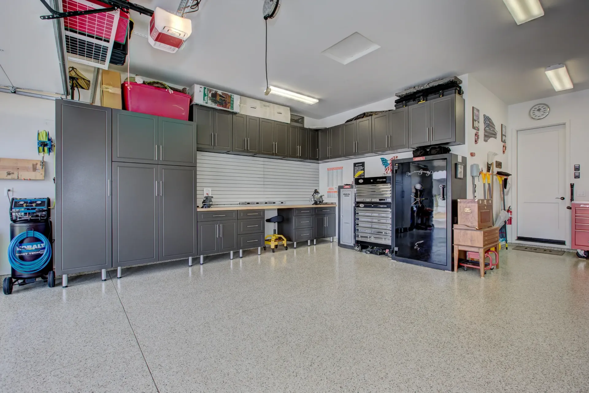 Spacious garage workshop with gray cabinets, workbench, tool storage, and a speckled epoxy floor