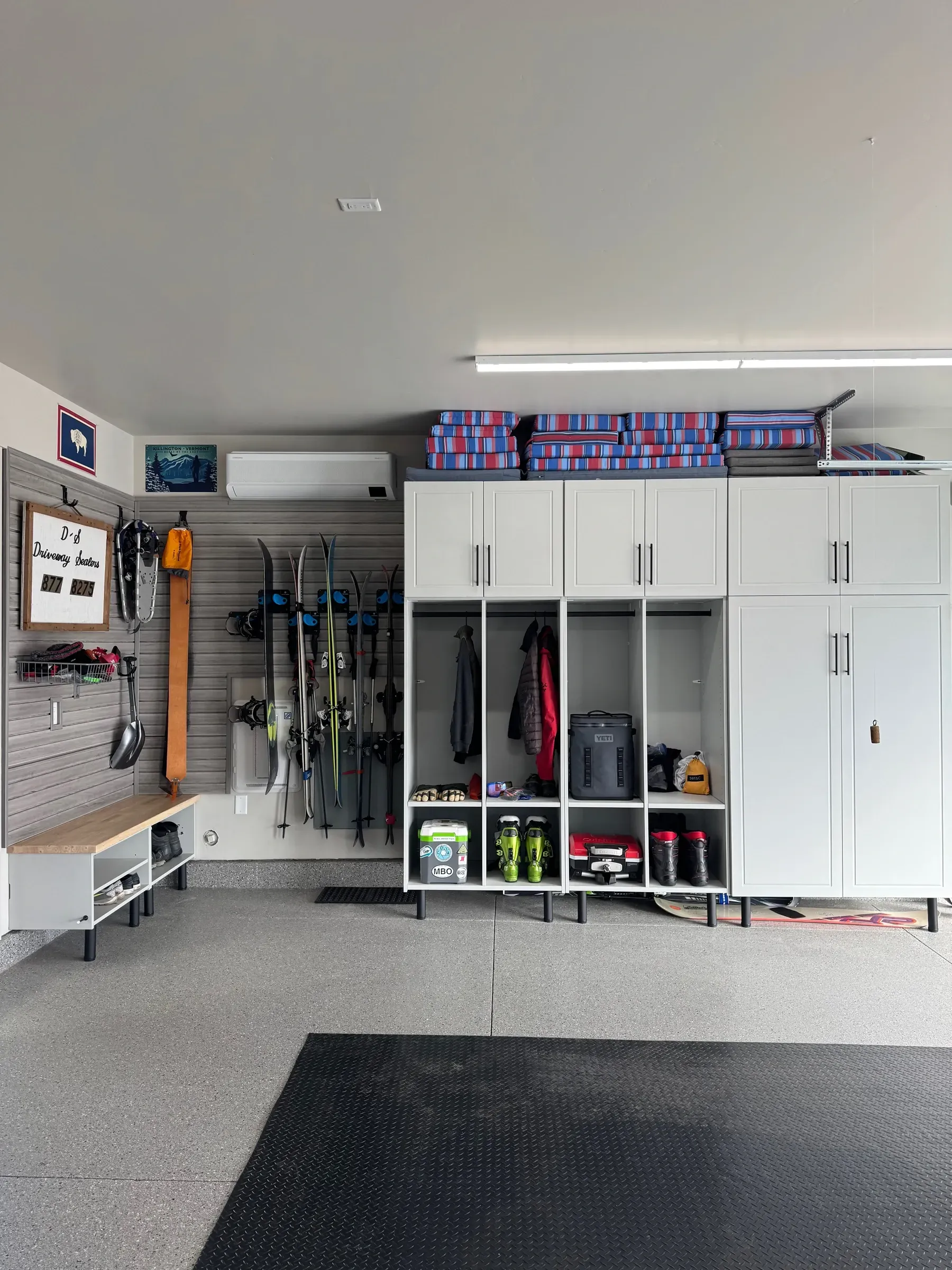 Garage with white storage cabinets, hanging tools, cleaning supplies, and a black floor mat on the concrete floor