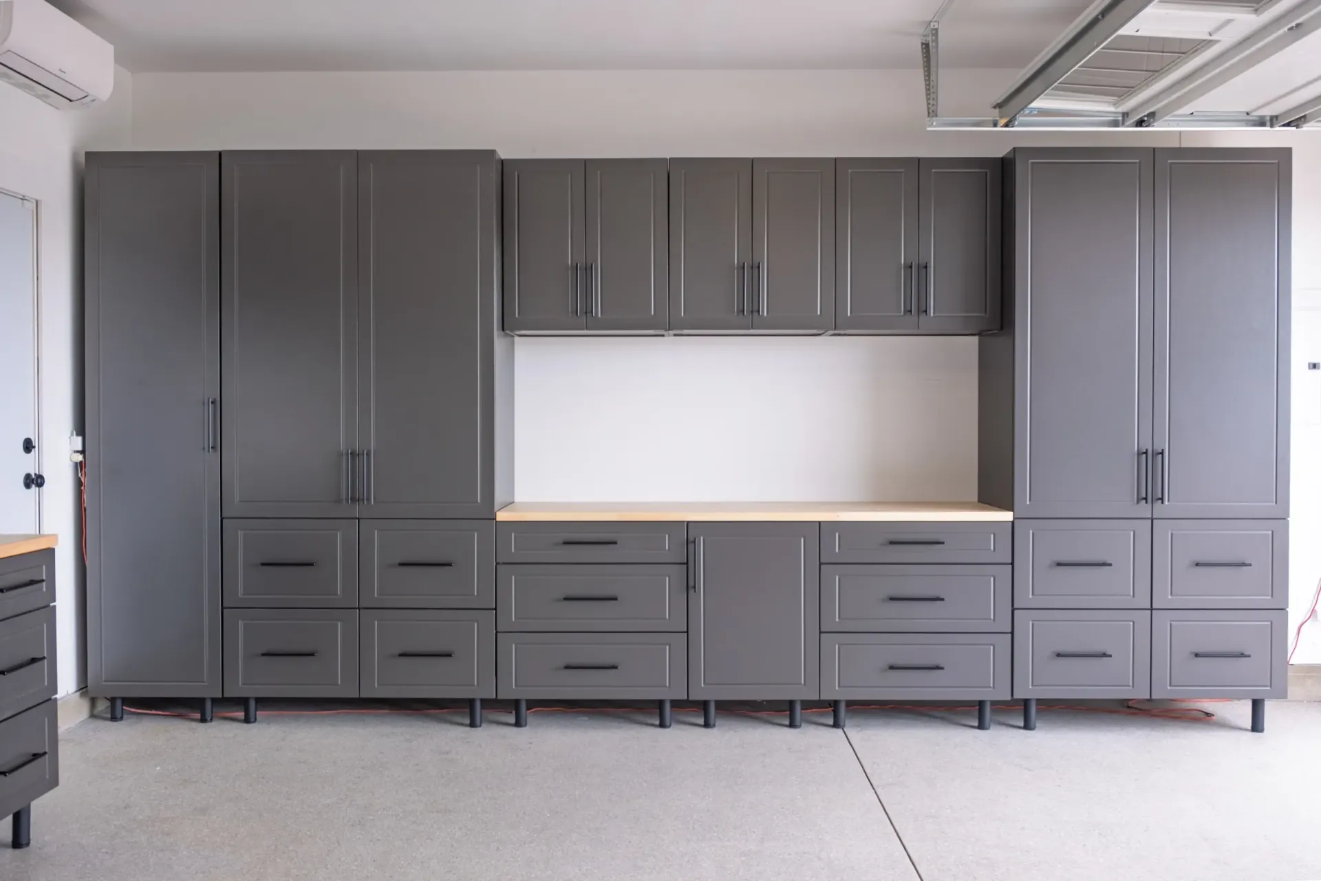 Gray wall-mounted garage cabinets with drawers and a white center panel across one wall