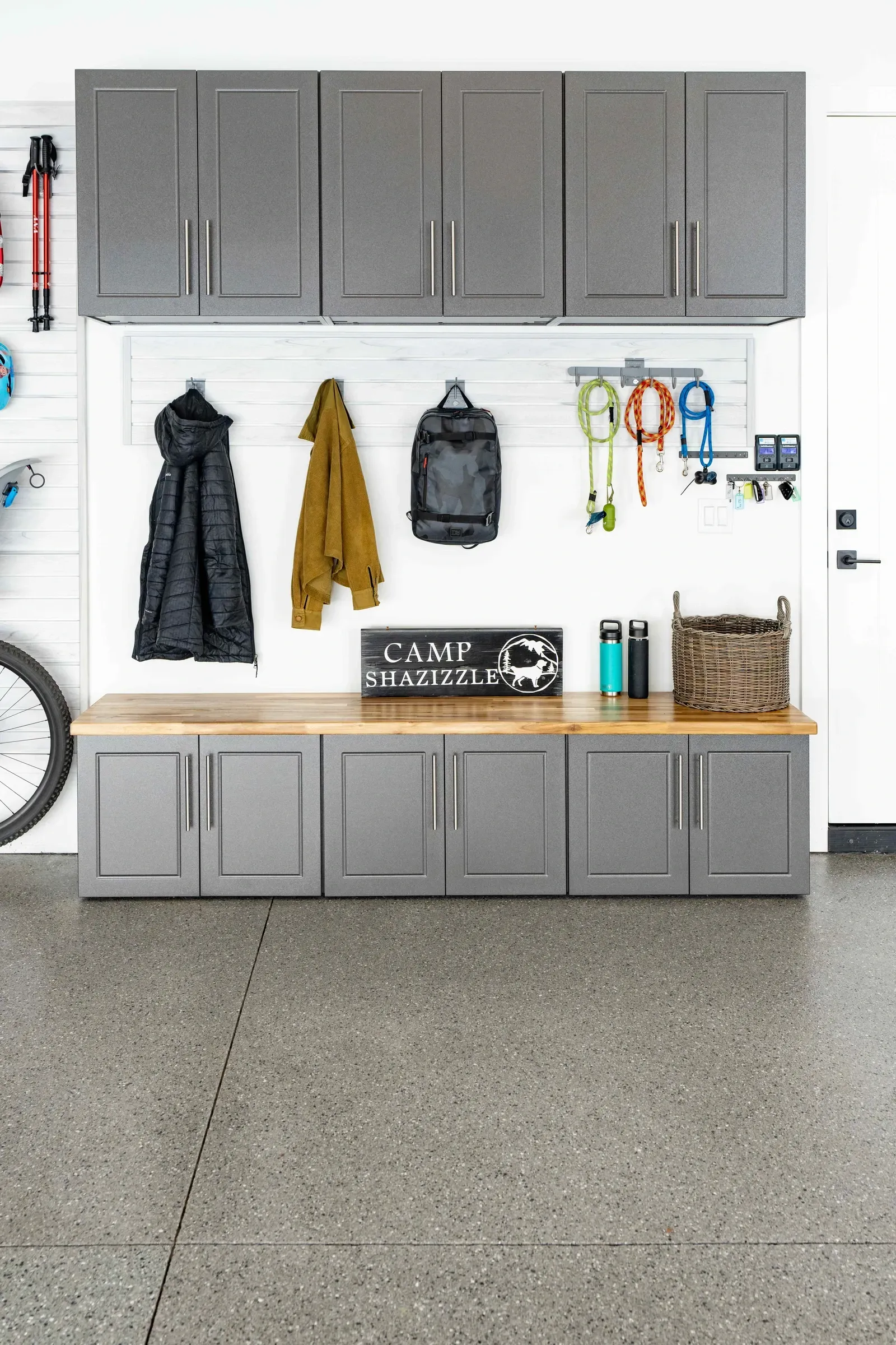 Garage storage wall with gray cabinets, hanging coats, tools, and a workbench against a white wall