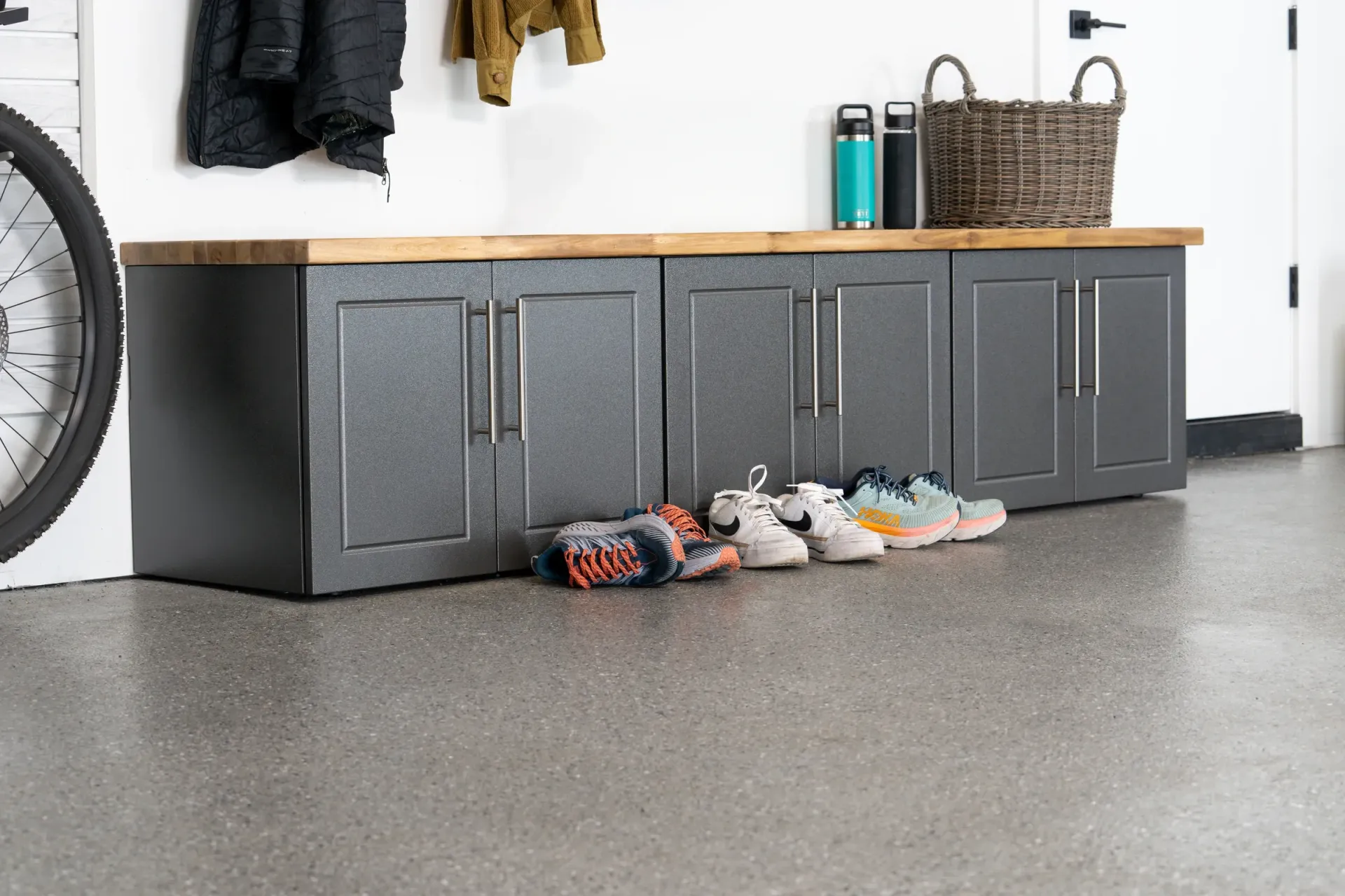 Gray garage cabinets with a wooden countertop and shoes lined up on the floor