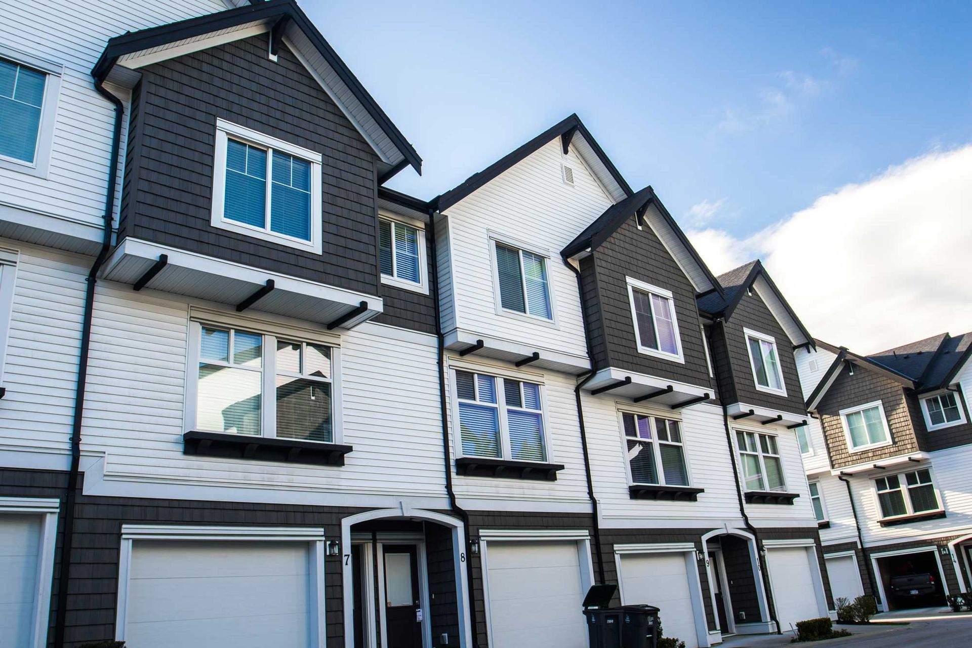 Row of modern white-and-gray townhouses with garages under a blue sky.