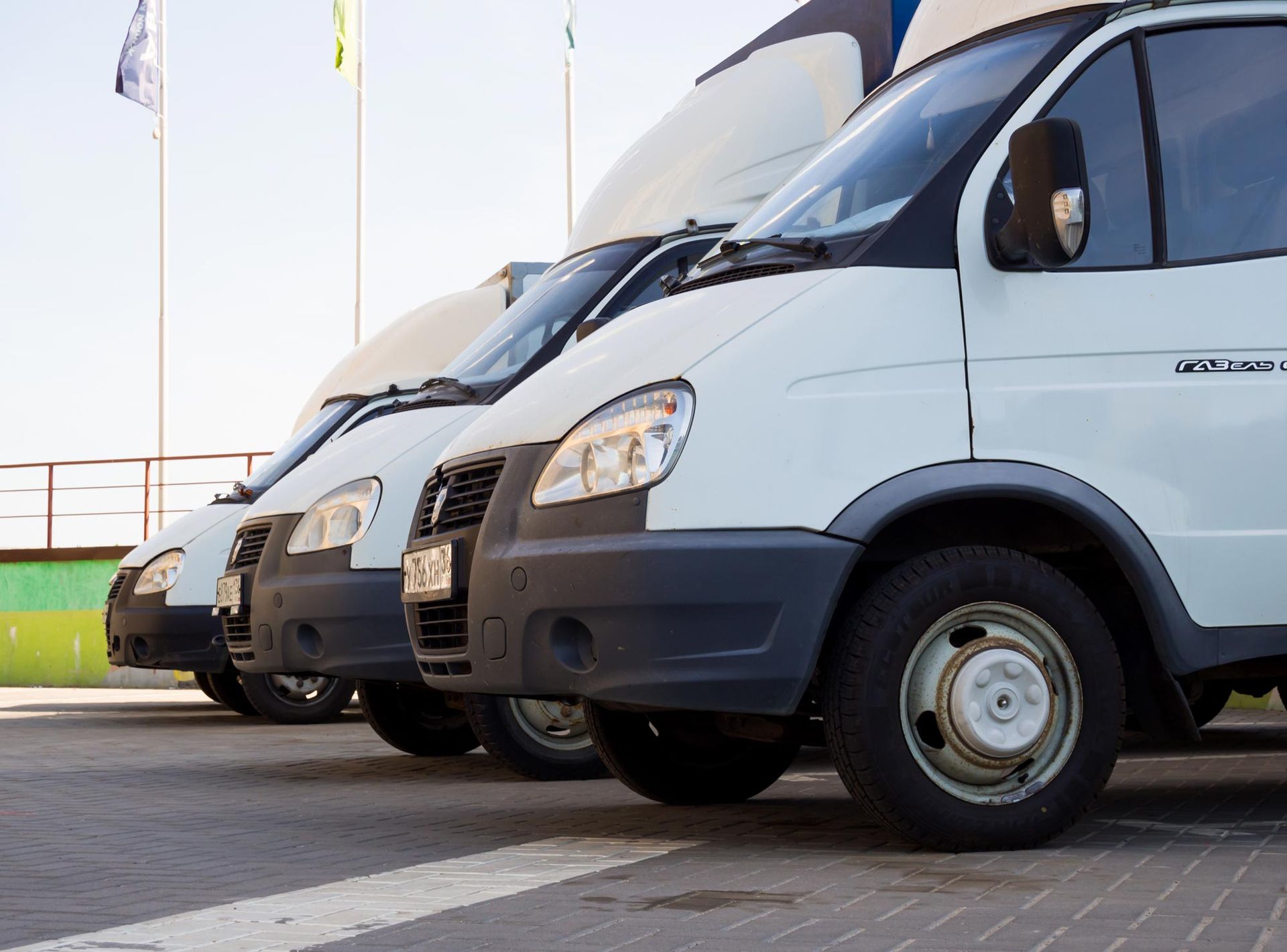 Three white delivery vans parked in a row outdoors near a curb.