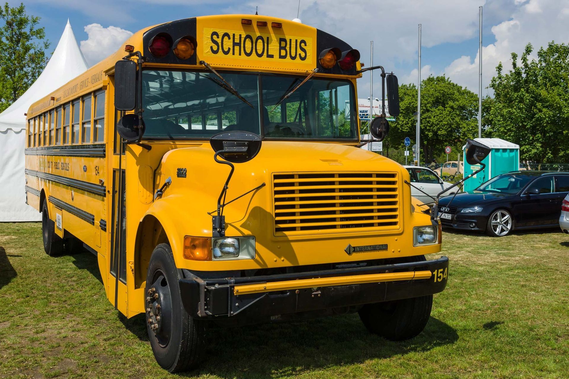Yellow school bus parked on grass near other vehicles under a partly cloudy sky