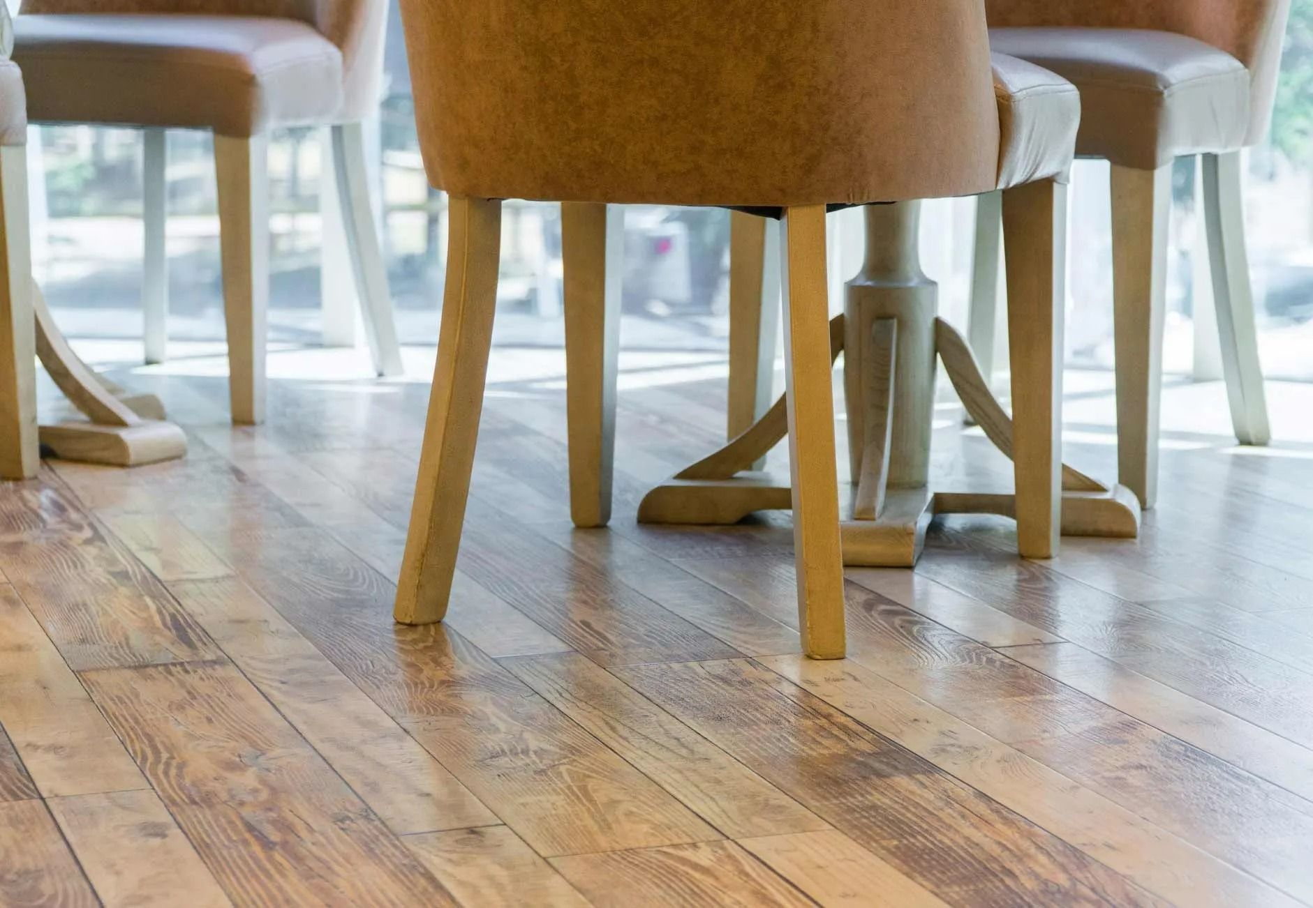 A low-angle view of several tan upholstered chairs with light wooden legs arranged on a polished hardwood floor.