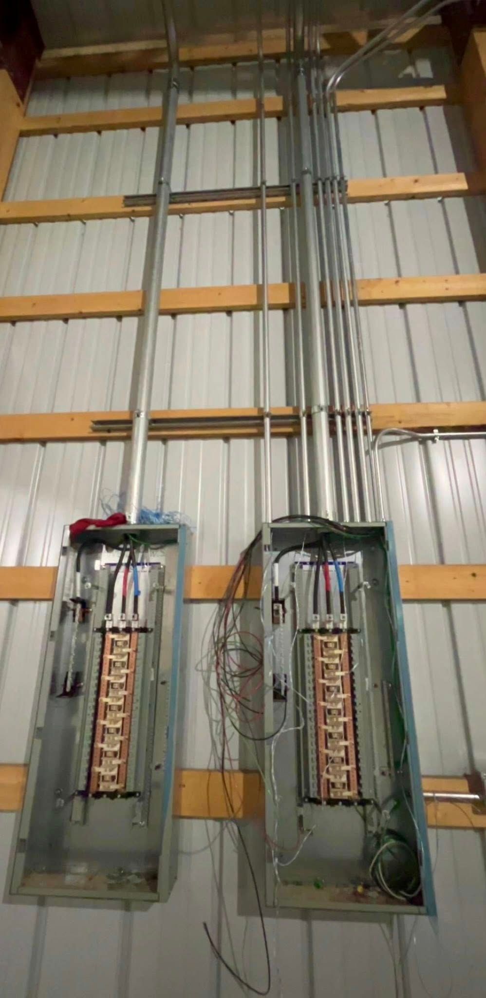 Two open electrical breaker panels mounted on a corrugated metal wall with metal conduits running upward.