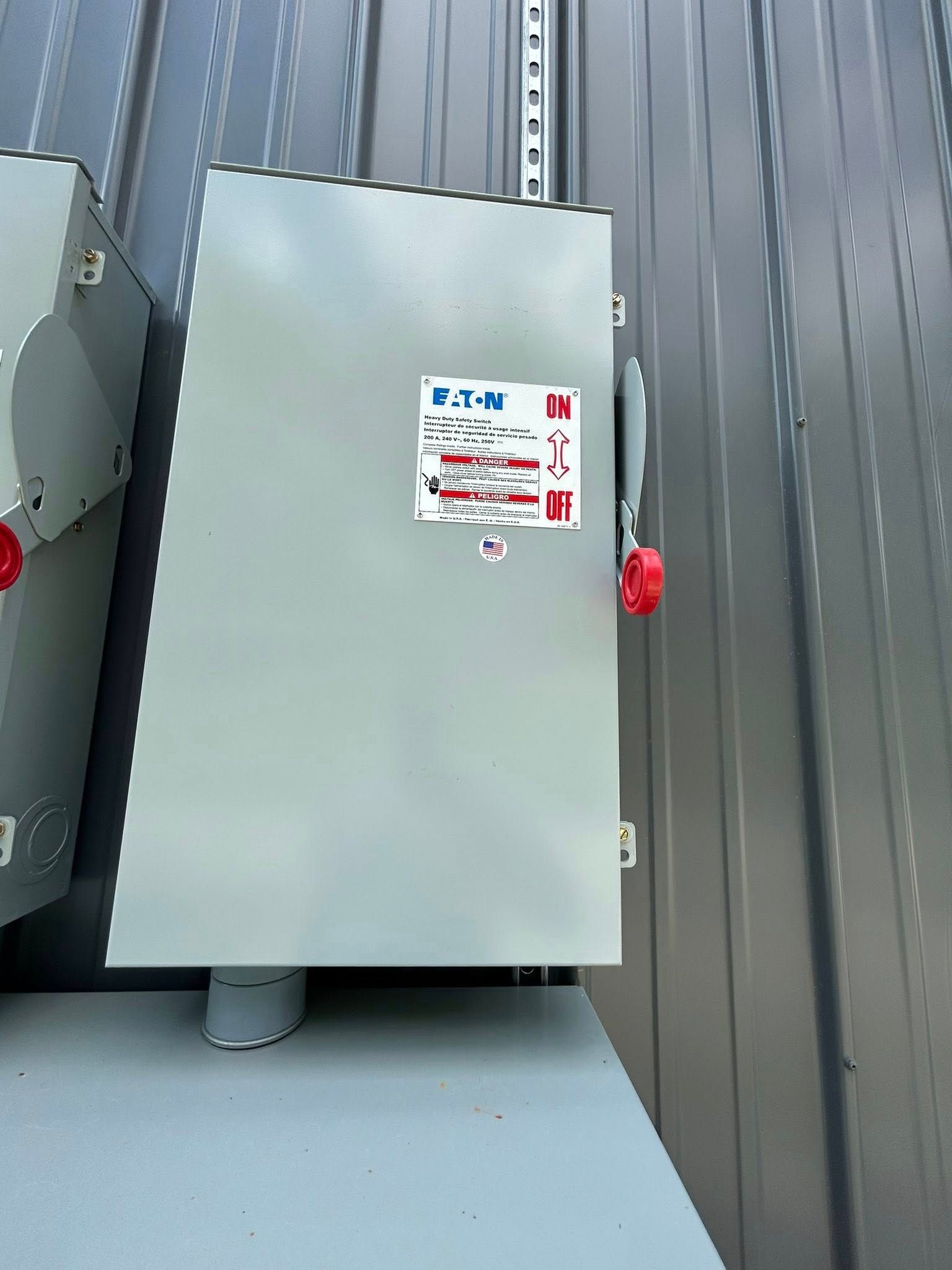 A grey, rectangular Eaton industrial electrical disconnect switch mounted on a corrugated metal wall.