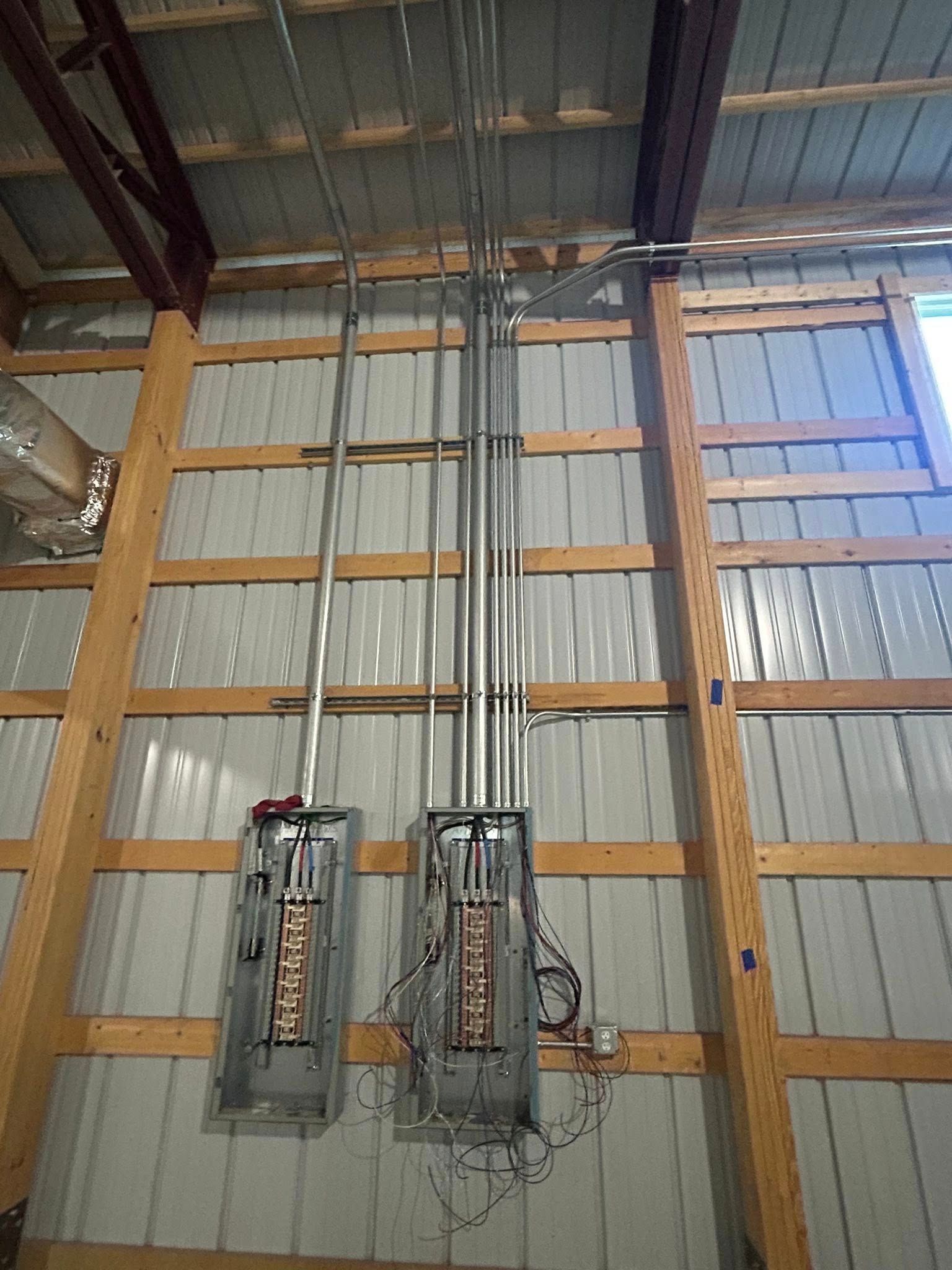 Two open electrical breaker panels mounted on a corrugated metal wall with vertical metal conduit running to the ceiling.