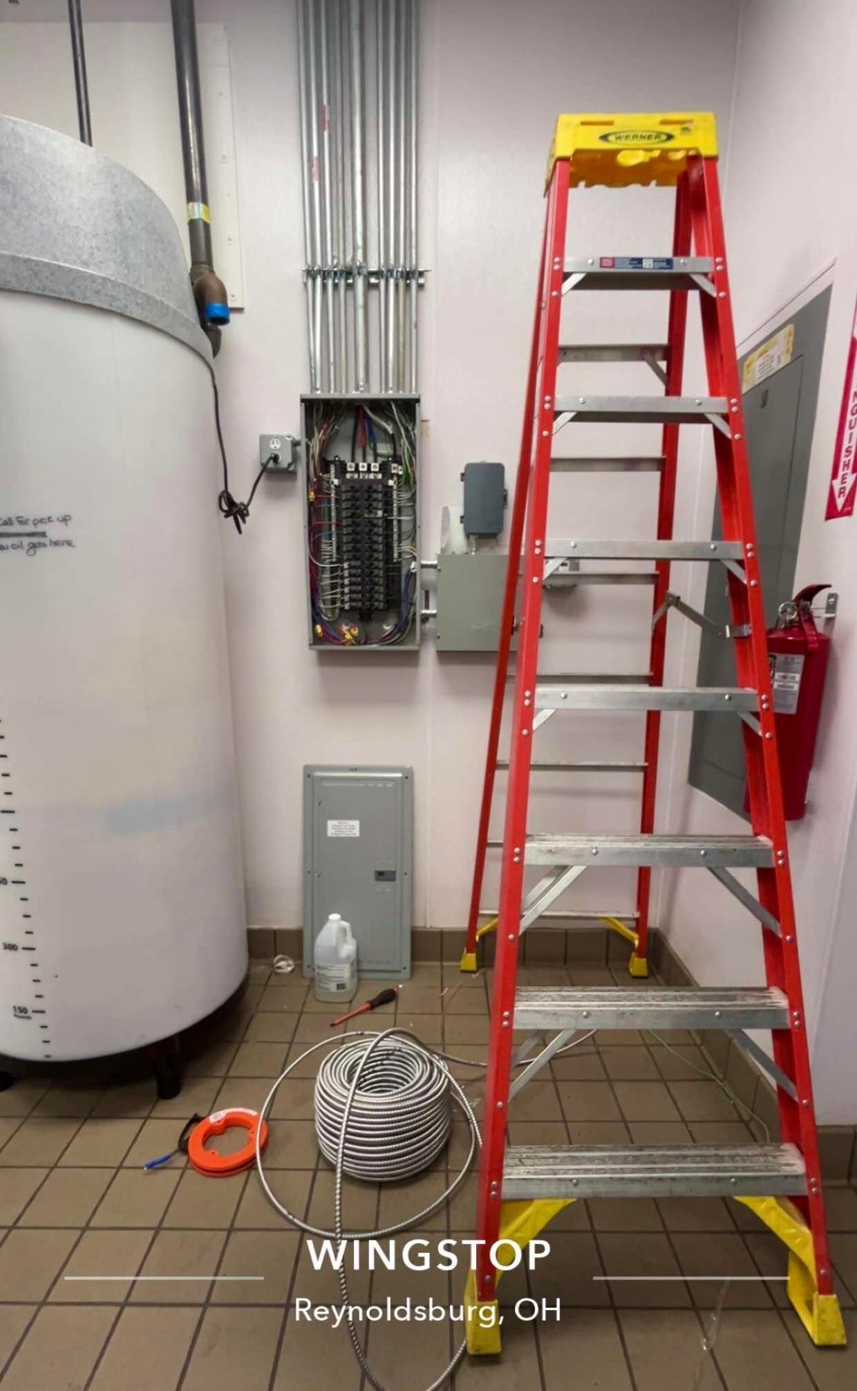 Electrical panel with an open cover and a ladder in a utility room at a Wingstop in Reynoldsburg, OH.