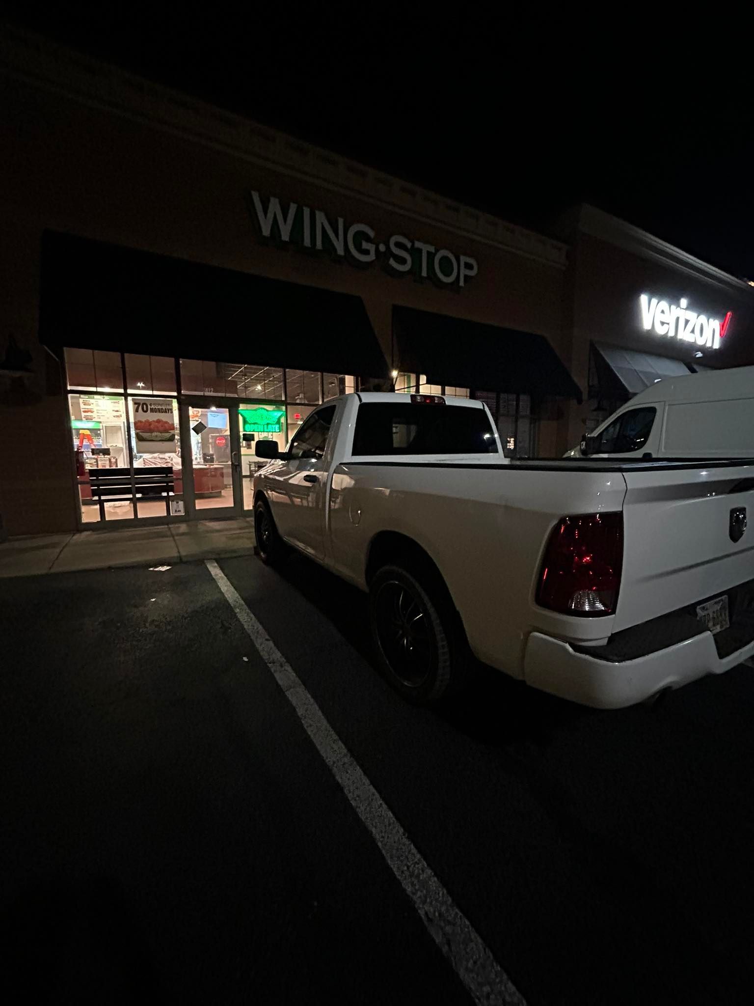 A white pickup truck parked in front of a Wingstop and Verizon storefront at night.