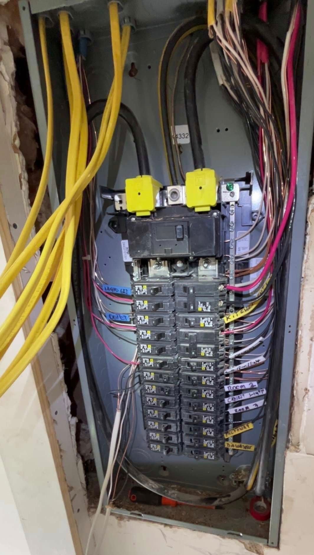 An open residential electrical breaker panel with multiple yellow-jacketed cables and various circuit breakers inside.