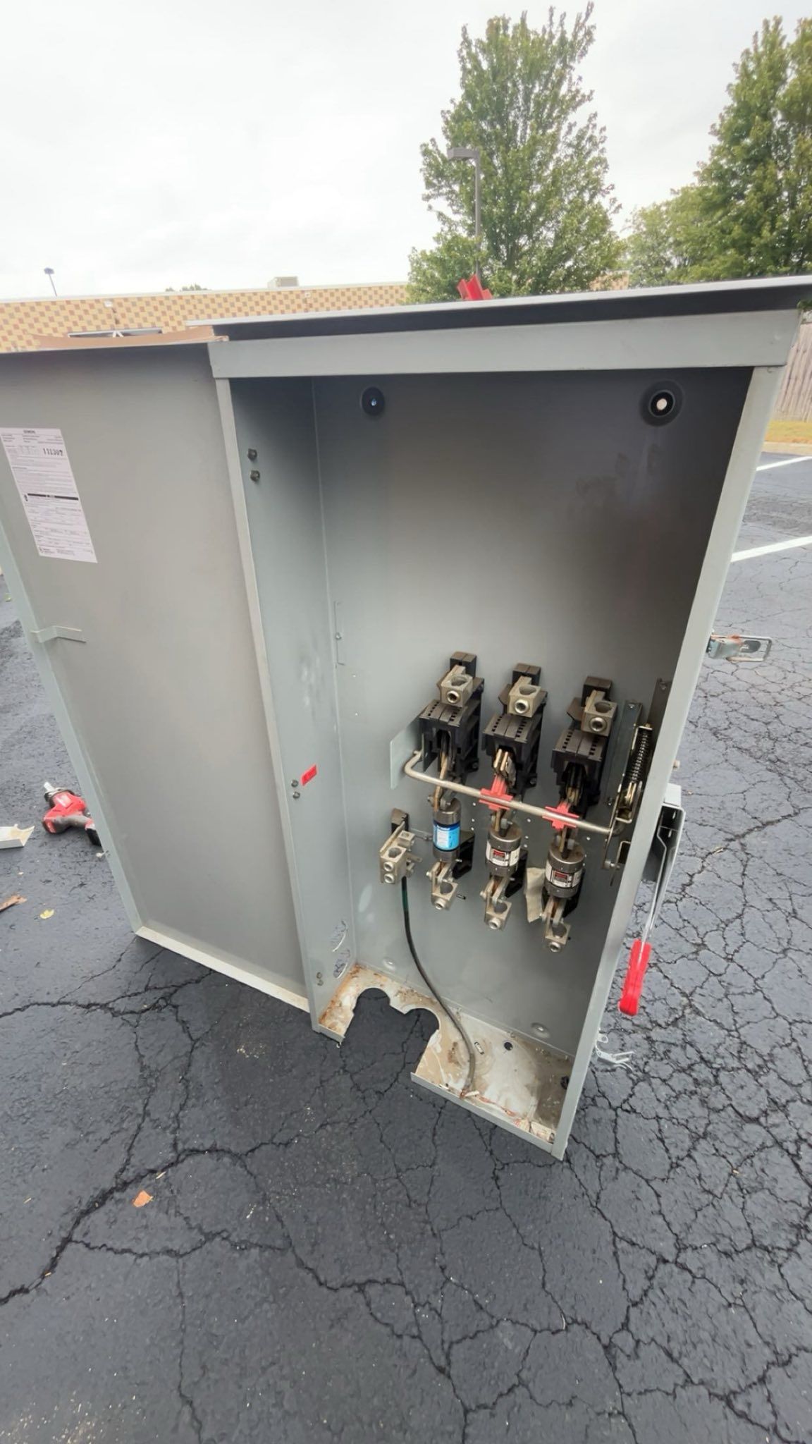 An open grey metal electrical utility cabinet featuring terminal blocks and wiring inside, situated on an asphalt surface.