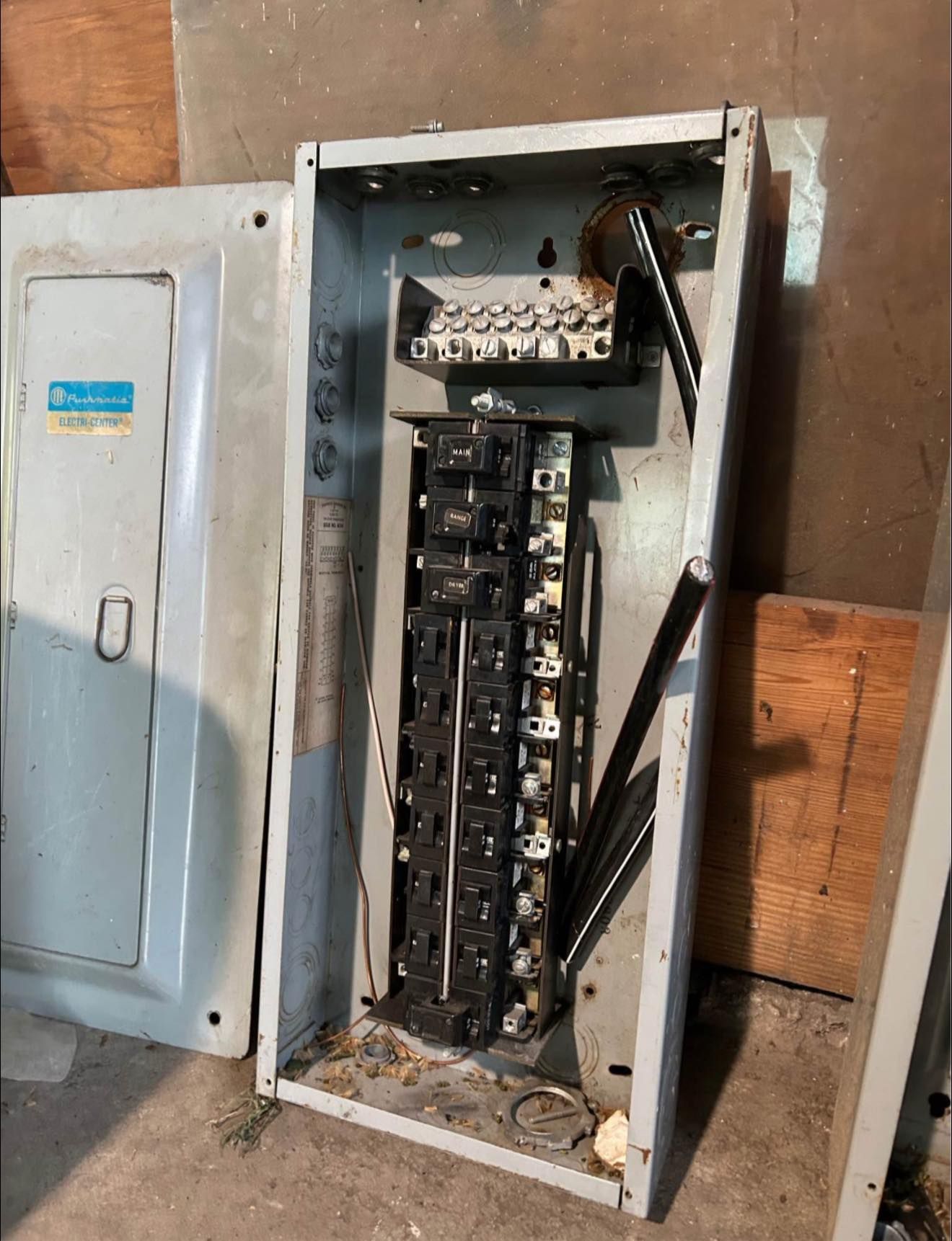 An open gray electrical panel box with breakers, mounted vertically against a wall.